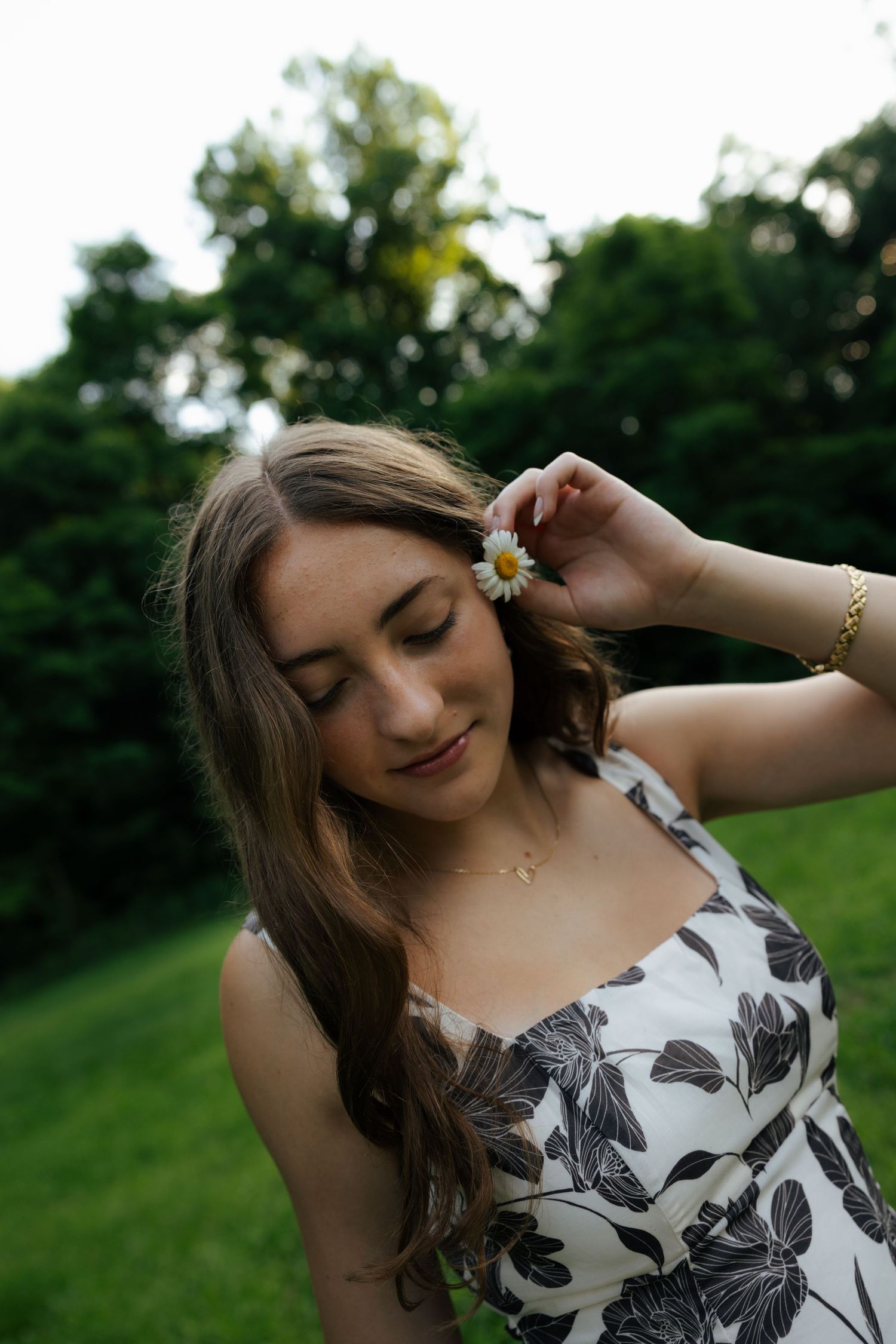 Young woman in floral dress placing a daisy in her hair outdoors.