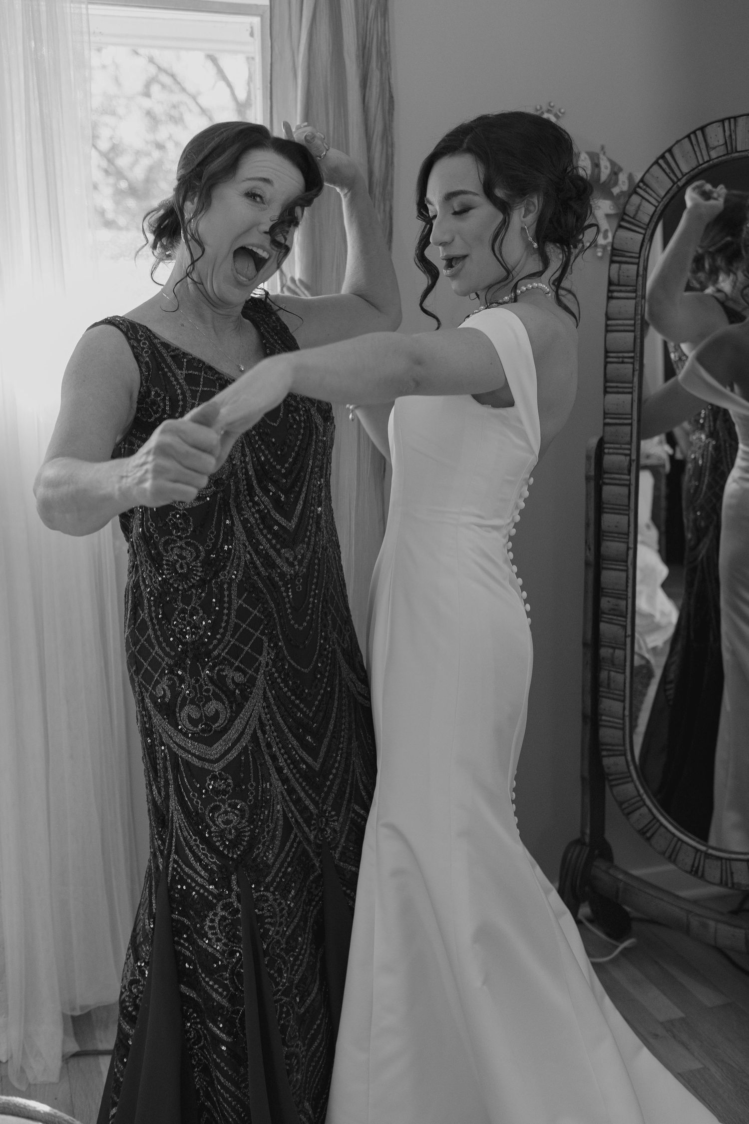 Black and white photo of bride and bridesmaid laughing together while getting ready for wedding.