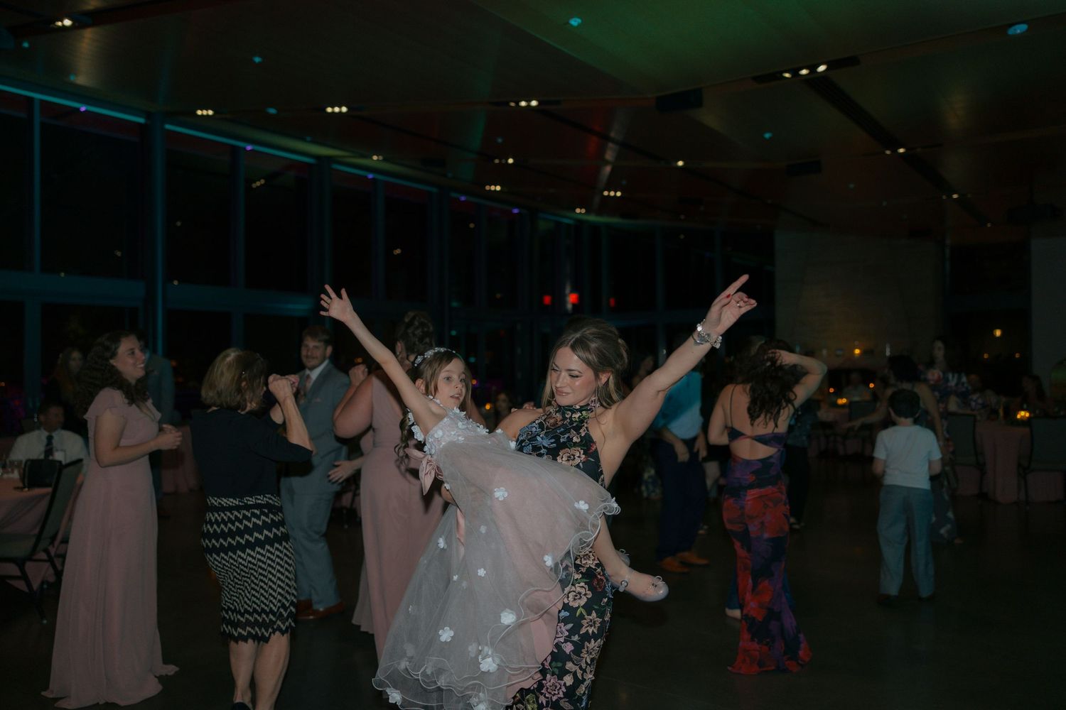 Guests dancing joyfully at an elegant evening reception with colorful lights in a modern venue.