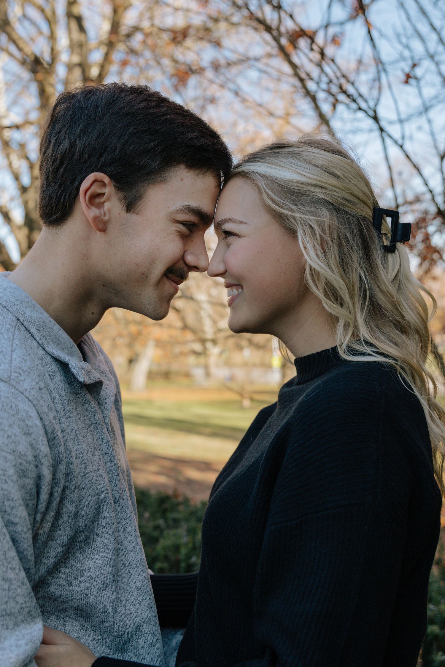 A romantic couple sharing intimate moments outdoors during autumn with bare trees in the background.