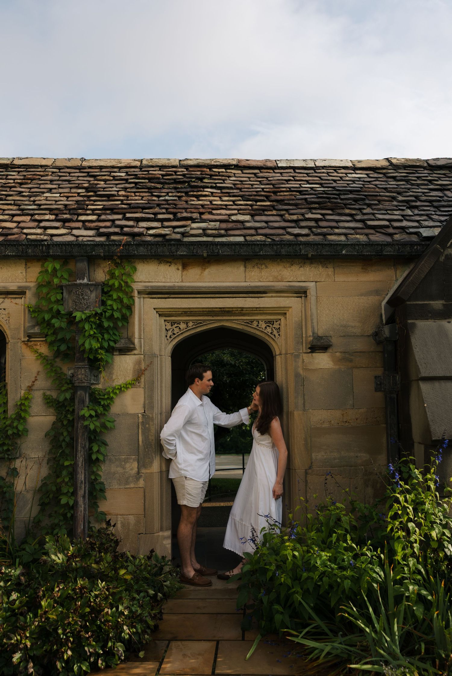 Romantic couple sharing a tender moment in Gothic stone archway covered in ivy.