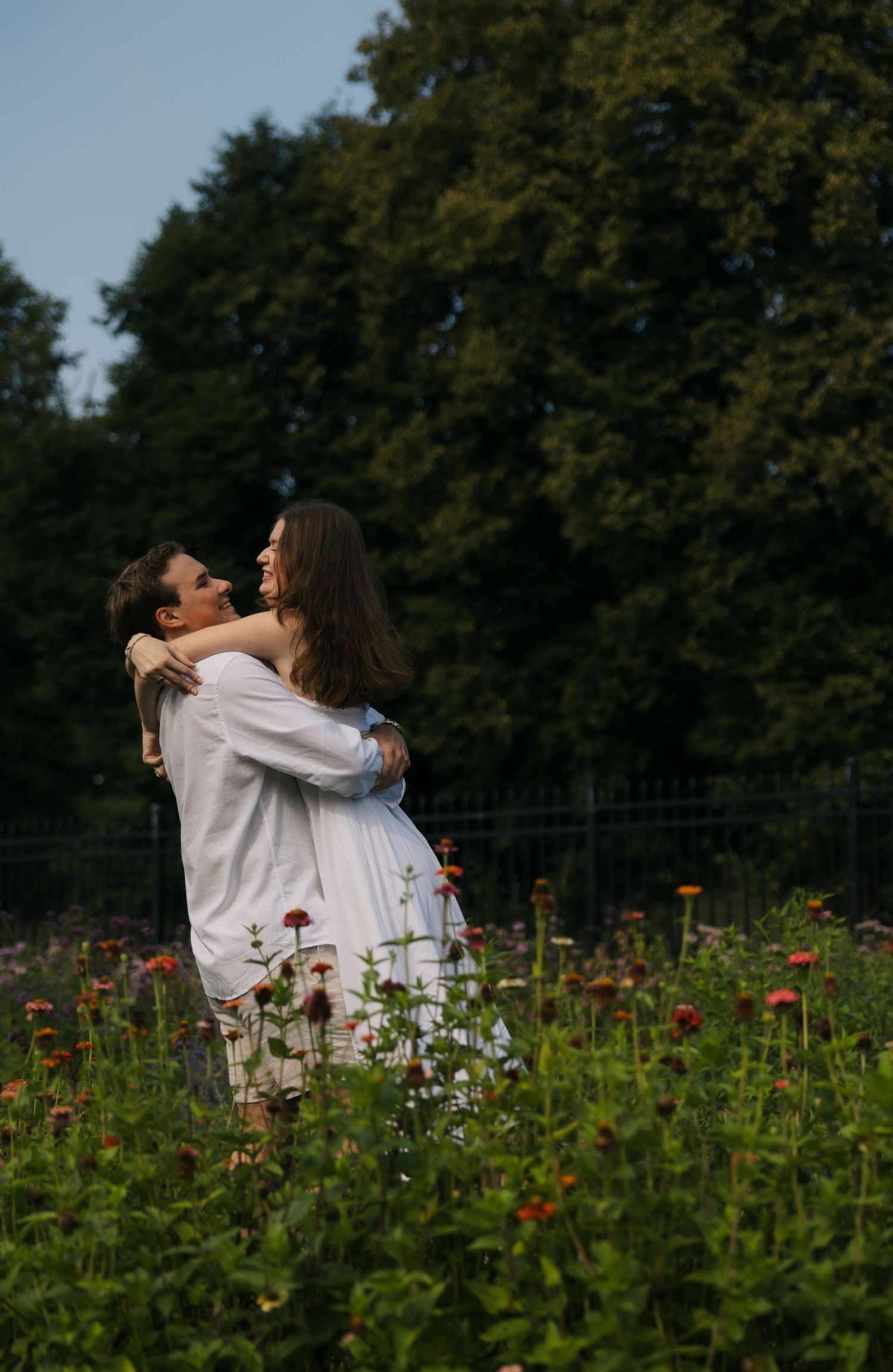 Couple embraces romantically in a vibrant flower garden surrounded by lush green trees.