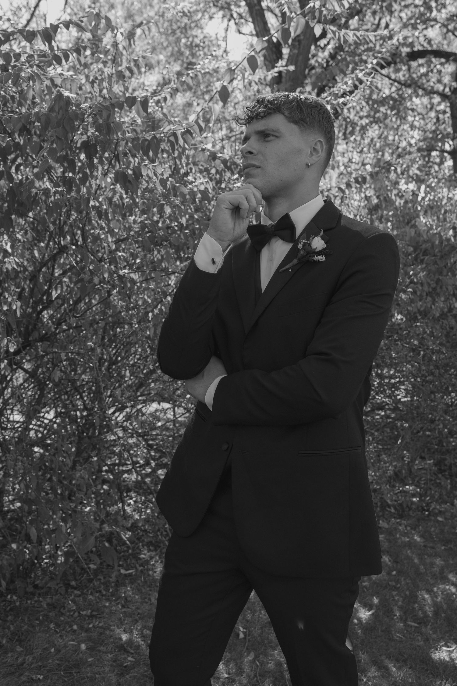 Black and white portrait of groom in tuxedo posing thoughtfully outdoors.