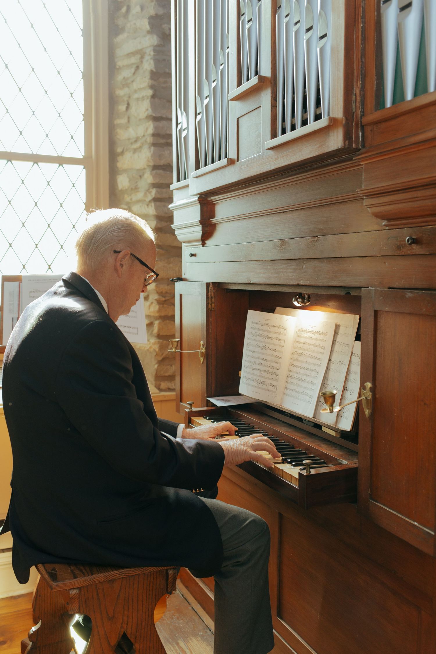 Elderly organist playing a pipe organ in a church, reading sheet music during a wedding ceremony.