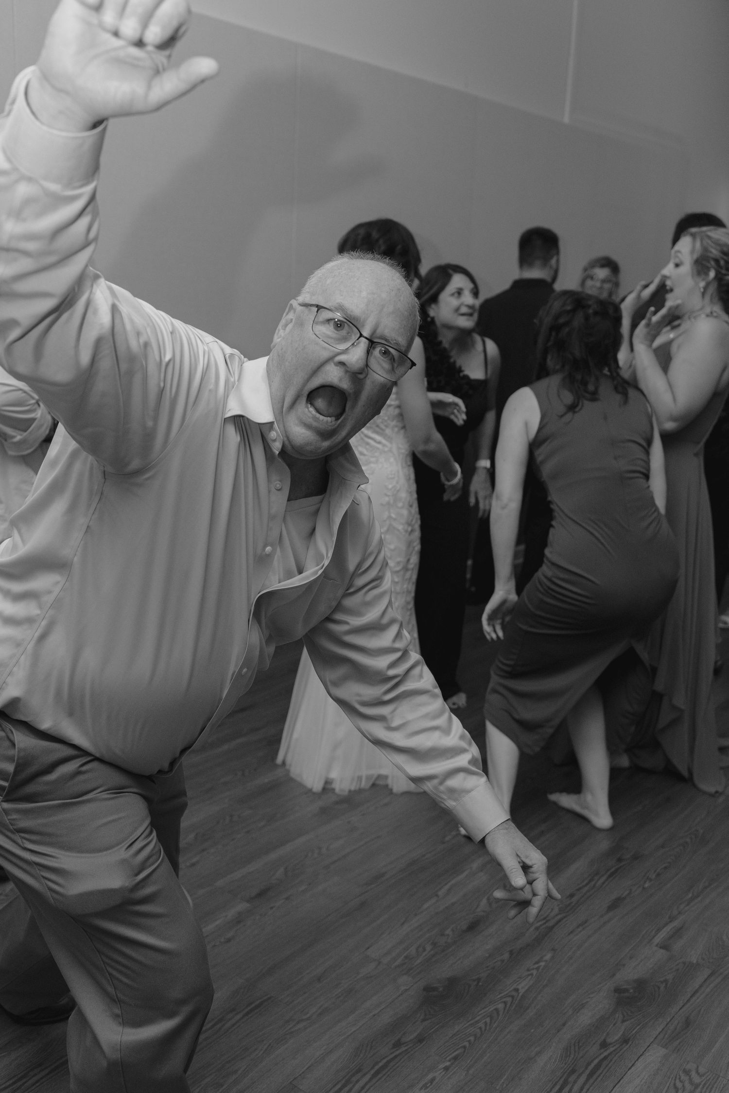 Energetic wedding guest dancing enthusiastically on reception dance floor in black and white photo.