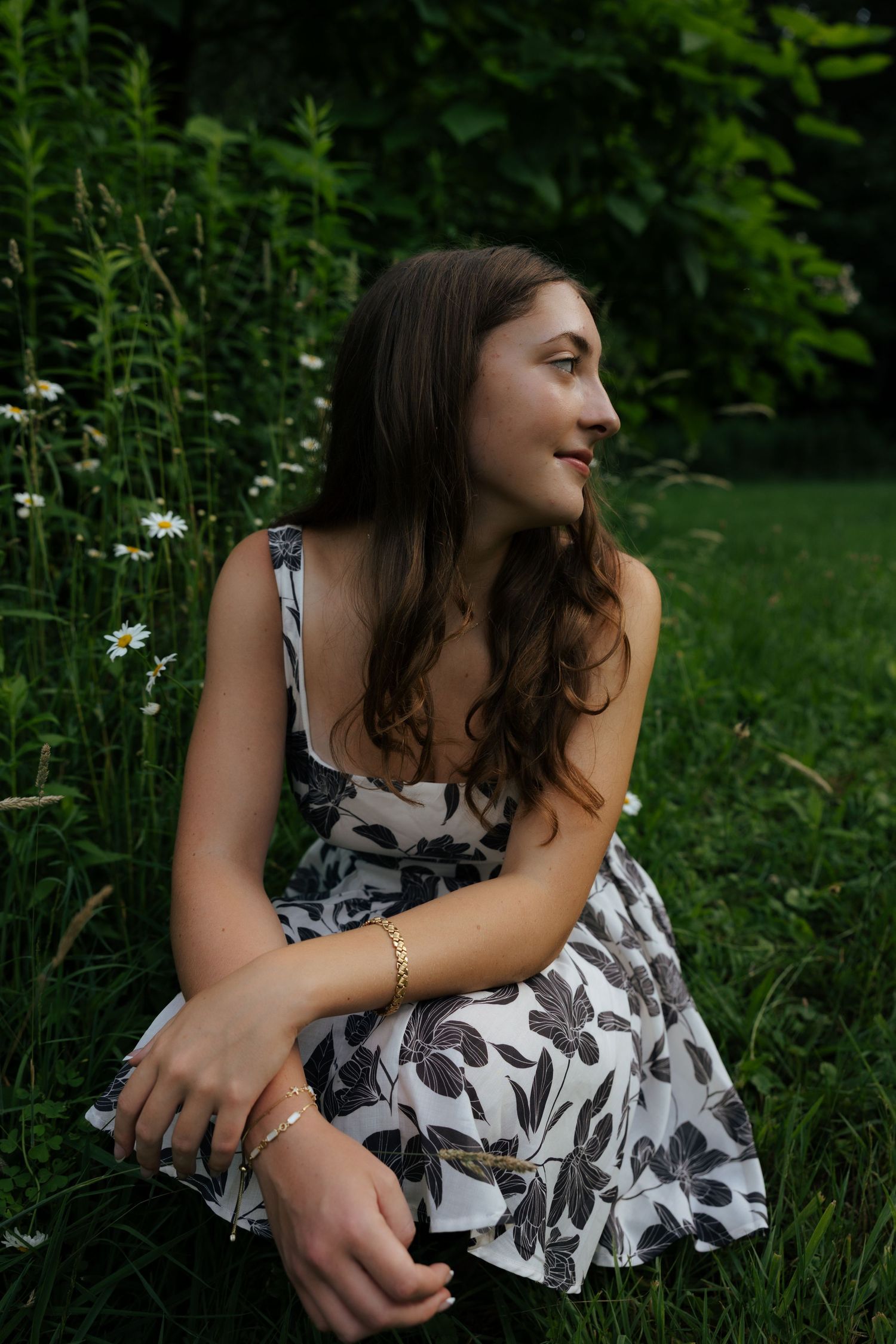Young woman in floral sundress sitting among wildflowers and green grass in a garden setting.