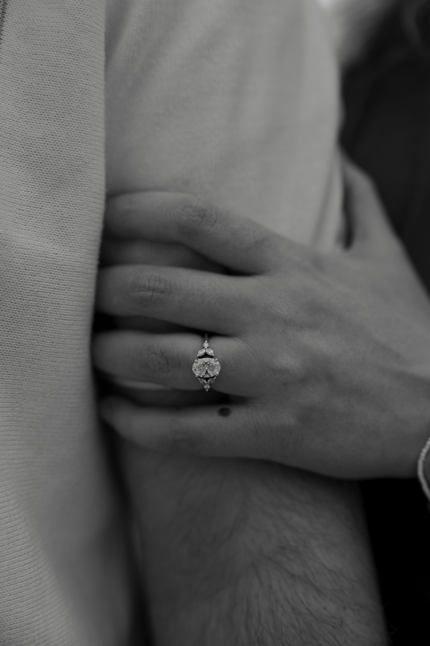 Close-up black and white photo of an engagement ring on a woman's hand as she embraces her partner.