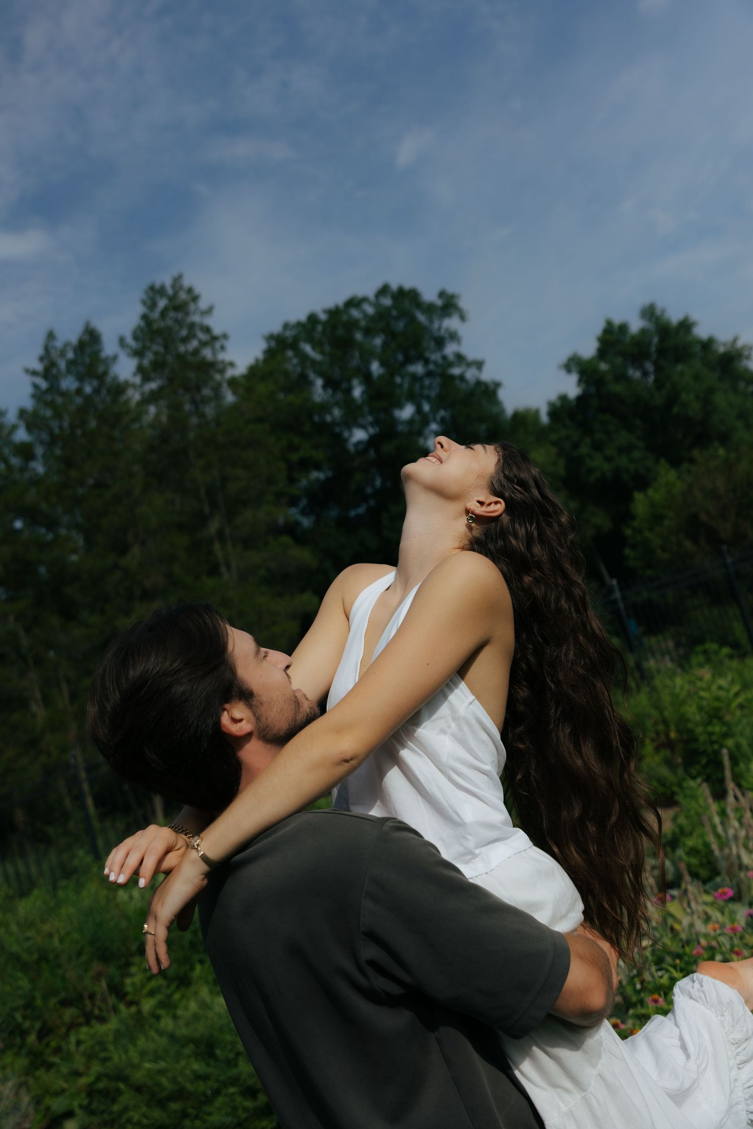 A couple shares a passionate moment outdoors, the woman leaning back with flowing hair under a bright blue sky.
