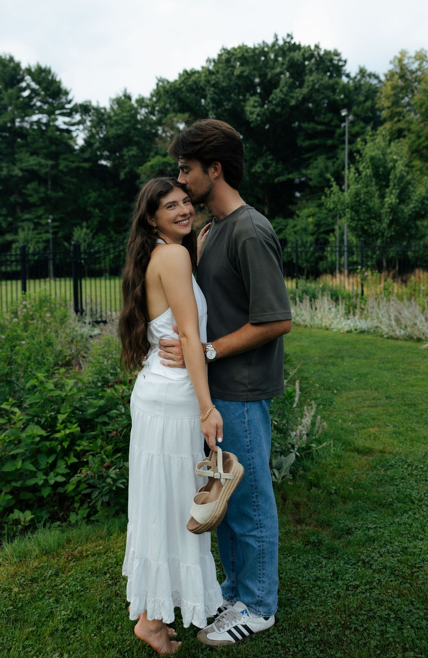 Couple embracing on a green lawn surrounded by lush garden plants on an overcast day.