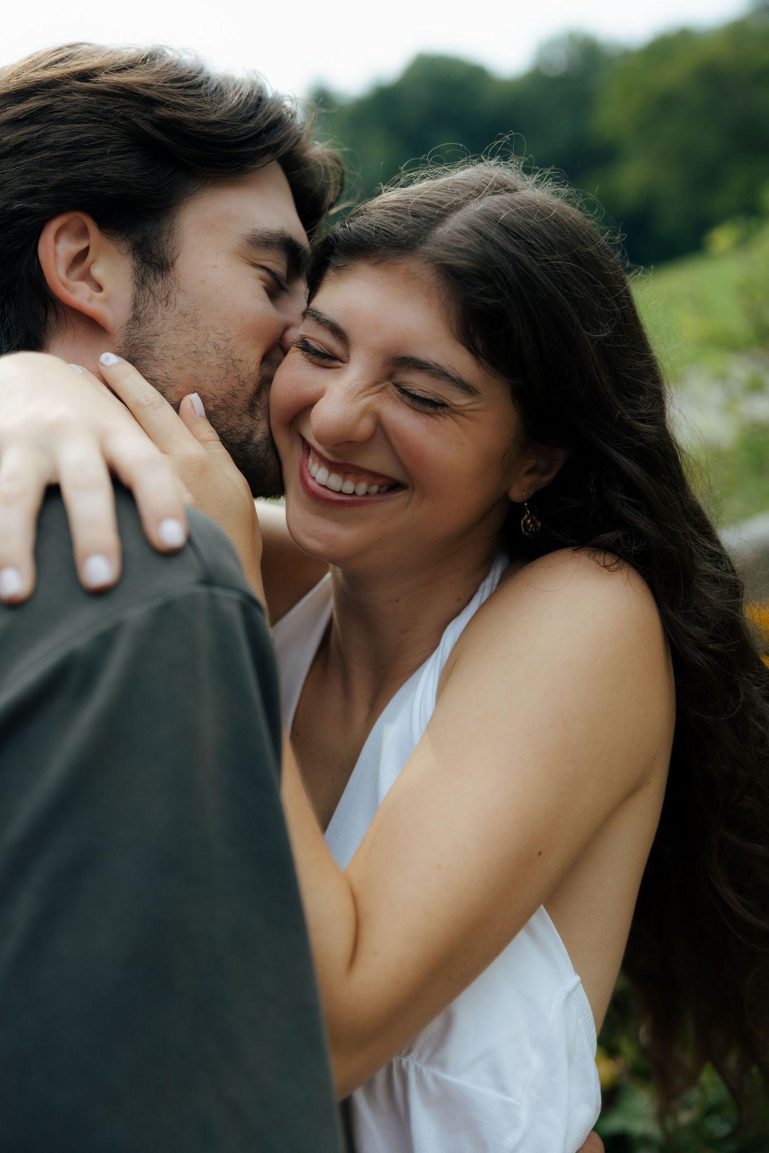 Happy woman laughing as man kisses her cheek outdoors in a romantic embrace.