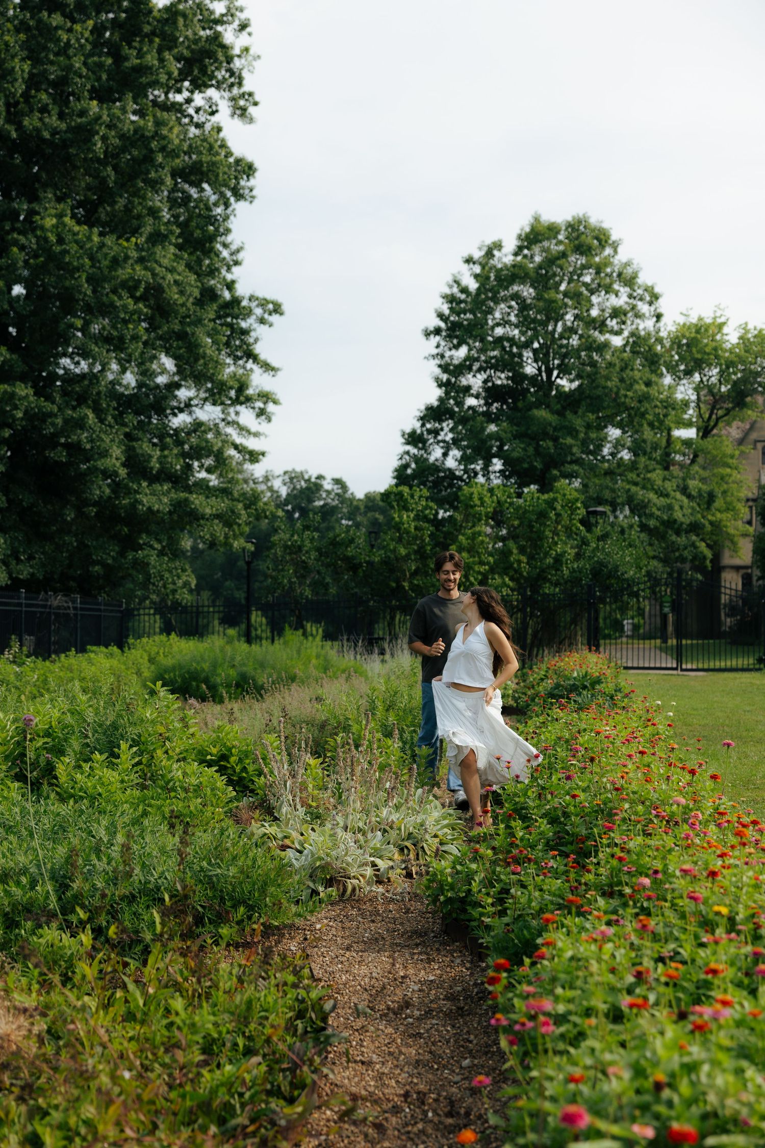 A couple embraces on a garden path surrounded by red flowers and lush greenery.