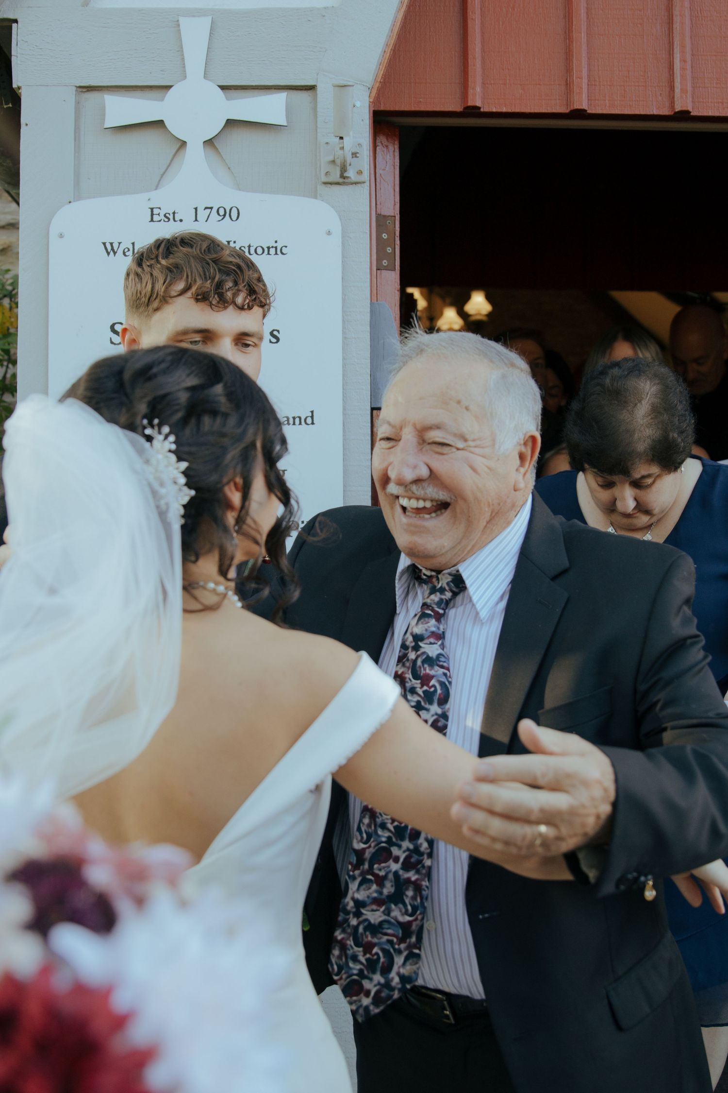 Joyful elderly man laughing while greeting the bride outside a historic church established in 1790.