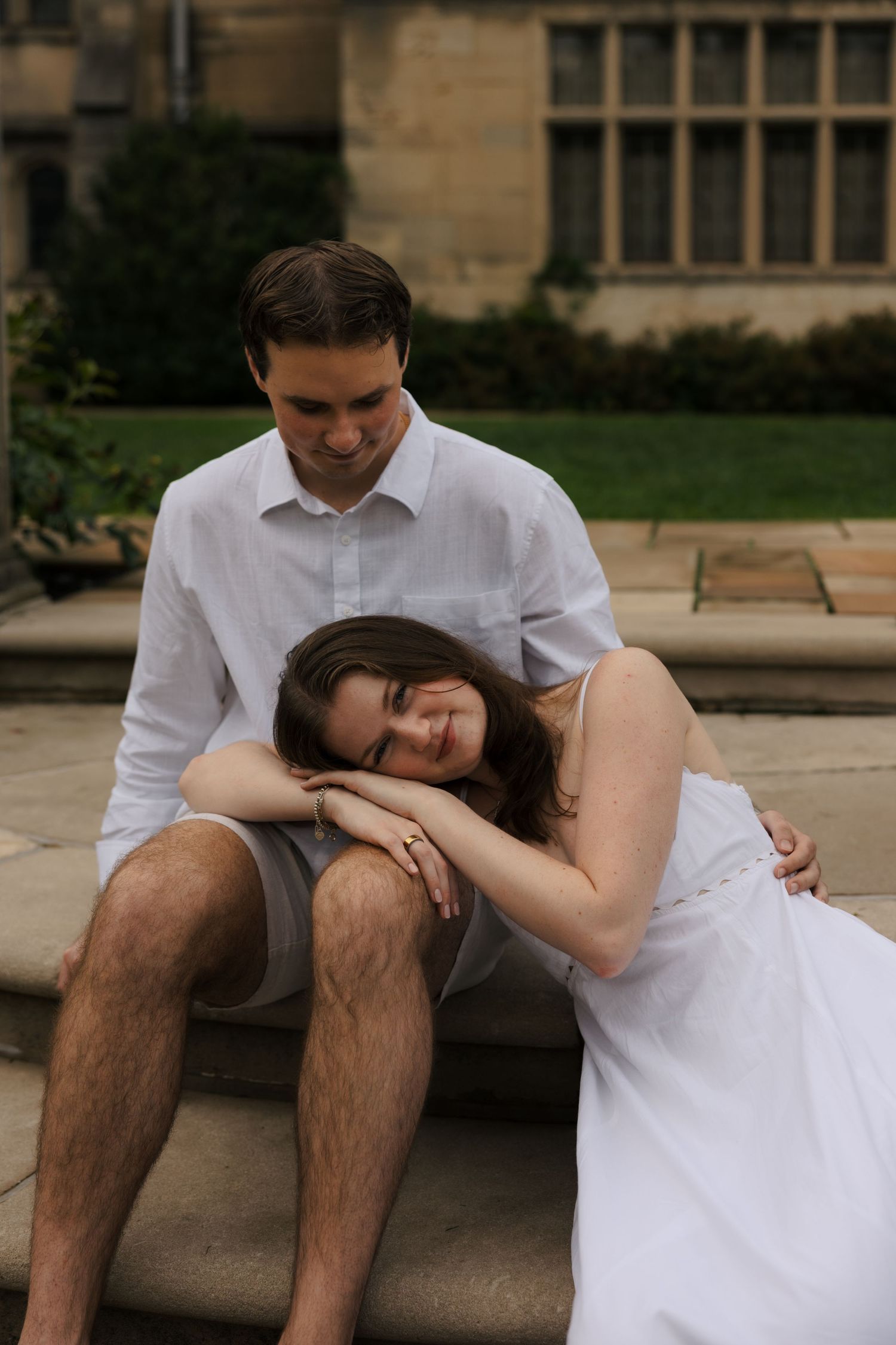 Couple in white sitting on stone steps, woman resting head on mans knee.