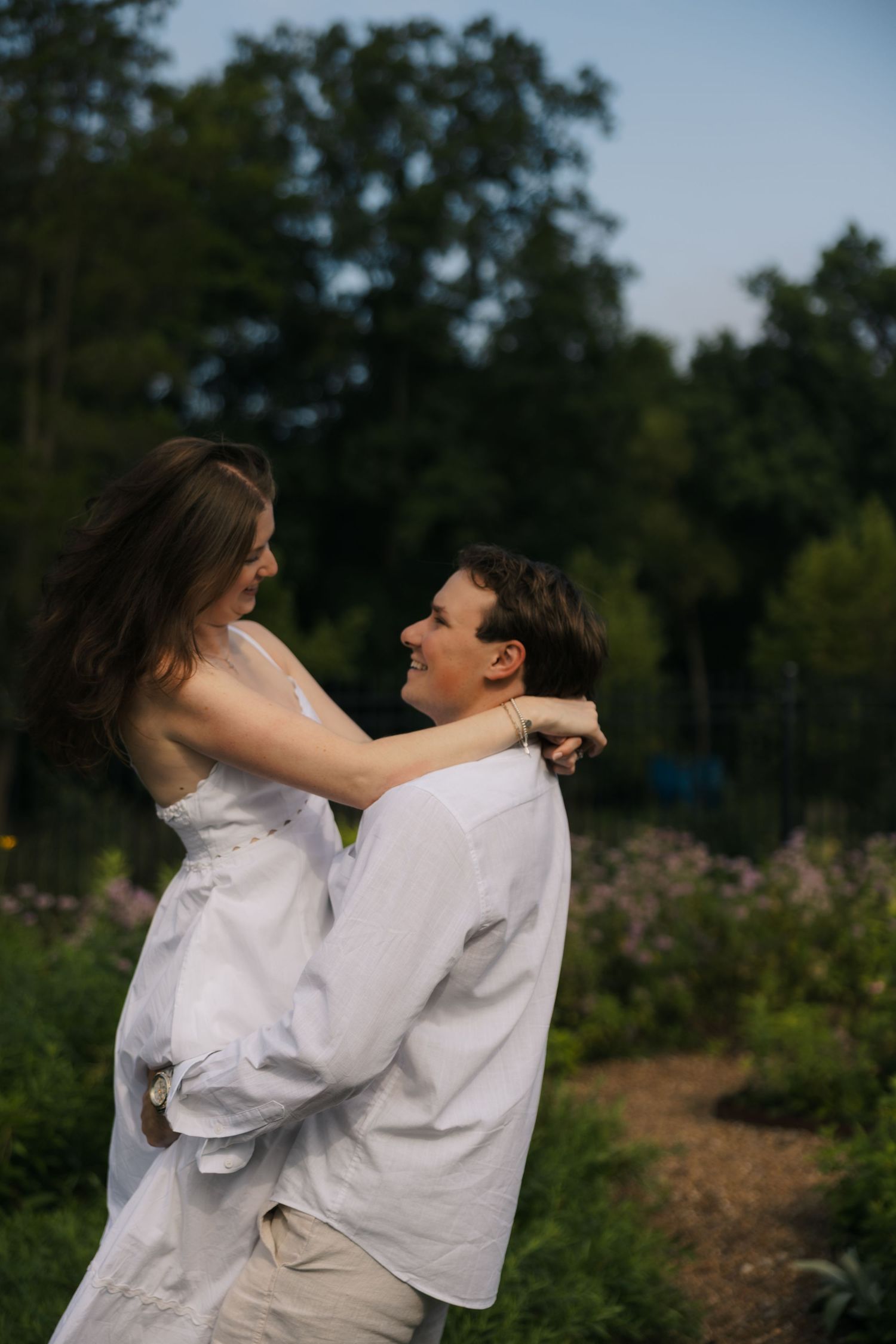 Couple embraces at golden hour in lush garden, woman wrapping arms around mans neck.