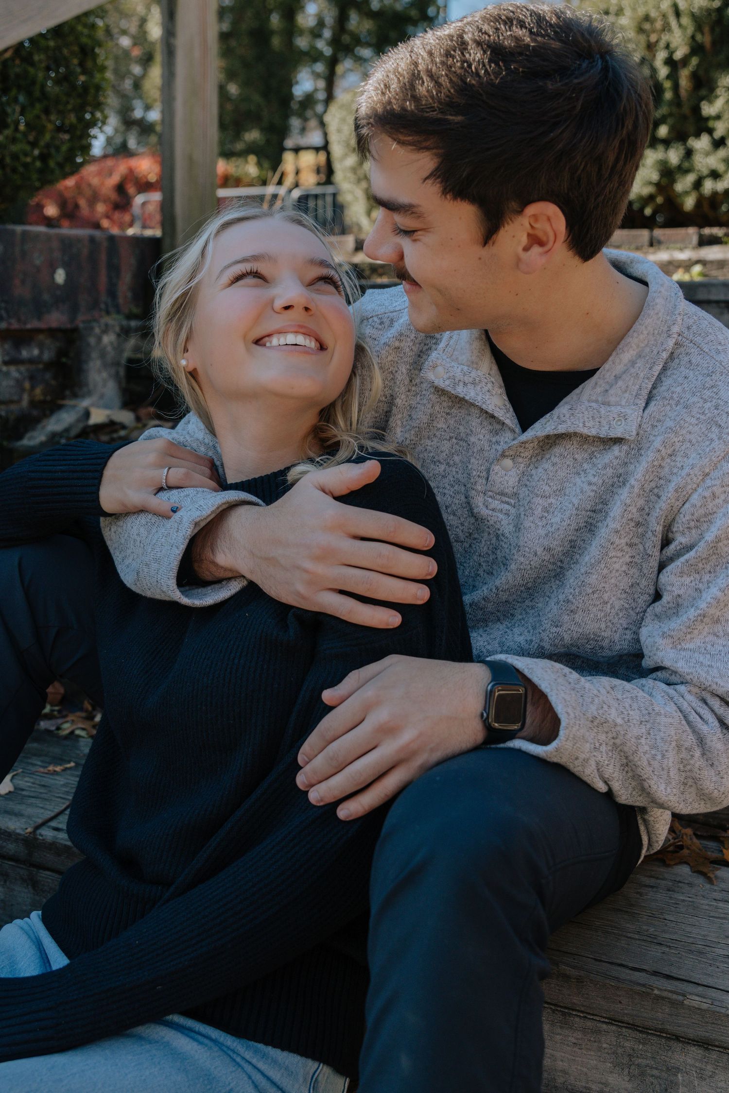 A couple sharing playful and affectionate moments while sitting on a wooden bench in a park setting.