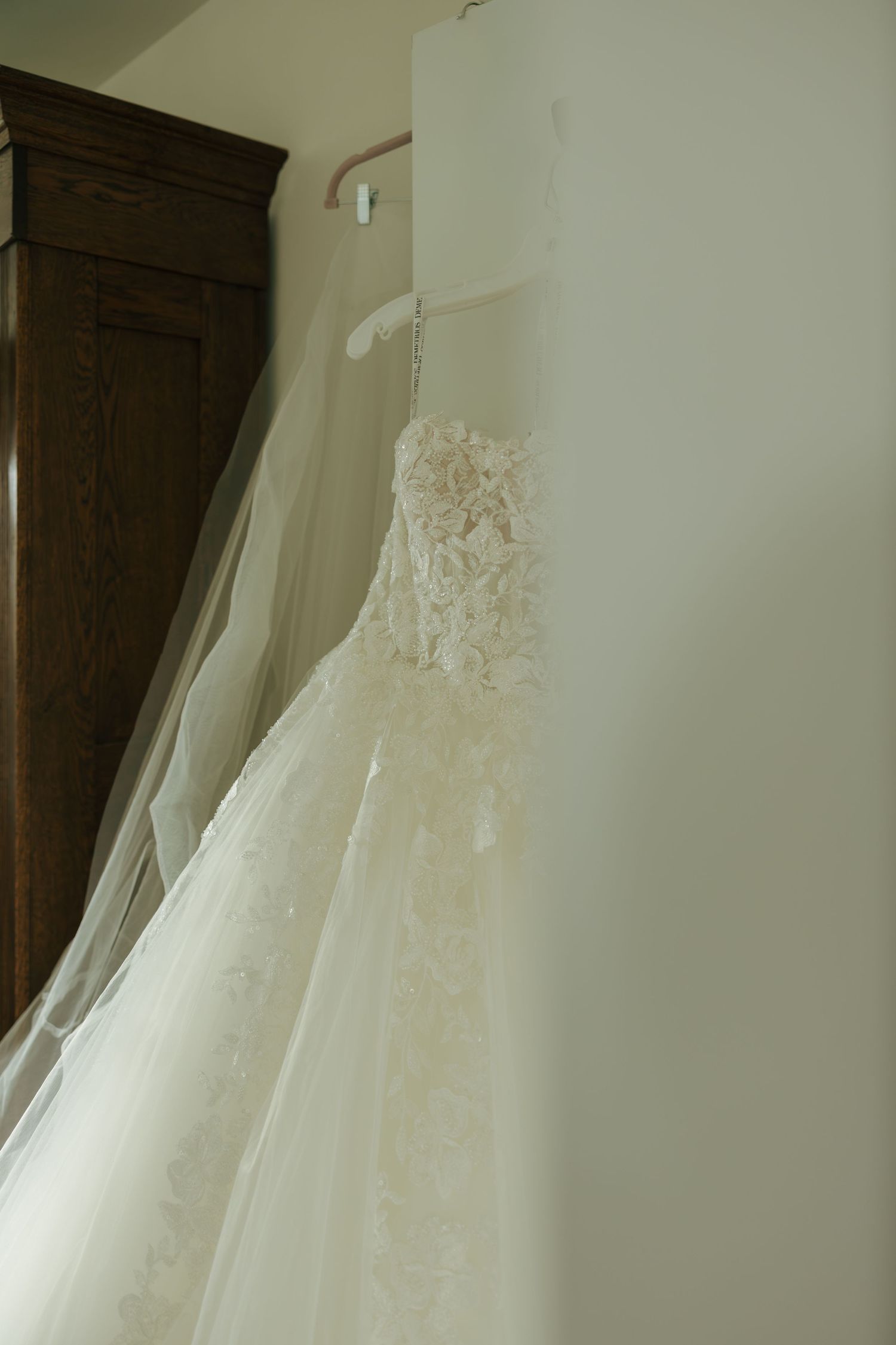 Elegant strapless lace wedding dress with floral appliques hanging on a white hanger against a cream wall.
