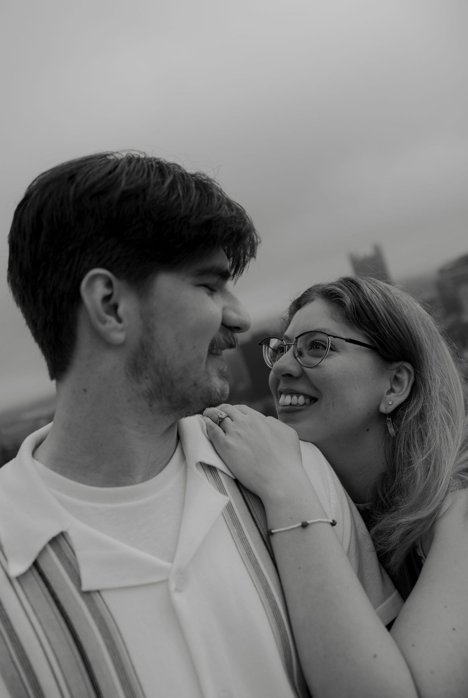 Black and white photo of a couple sharing a tender moment with a city skyline in the background.