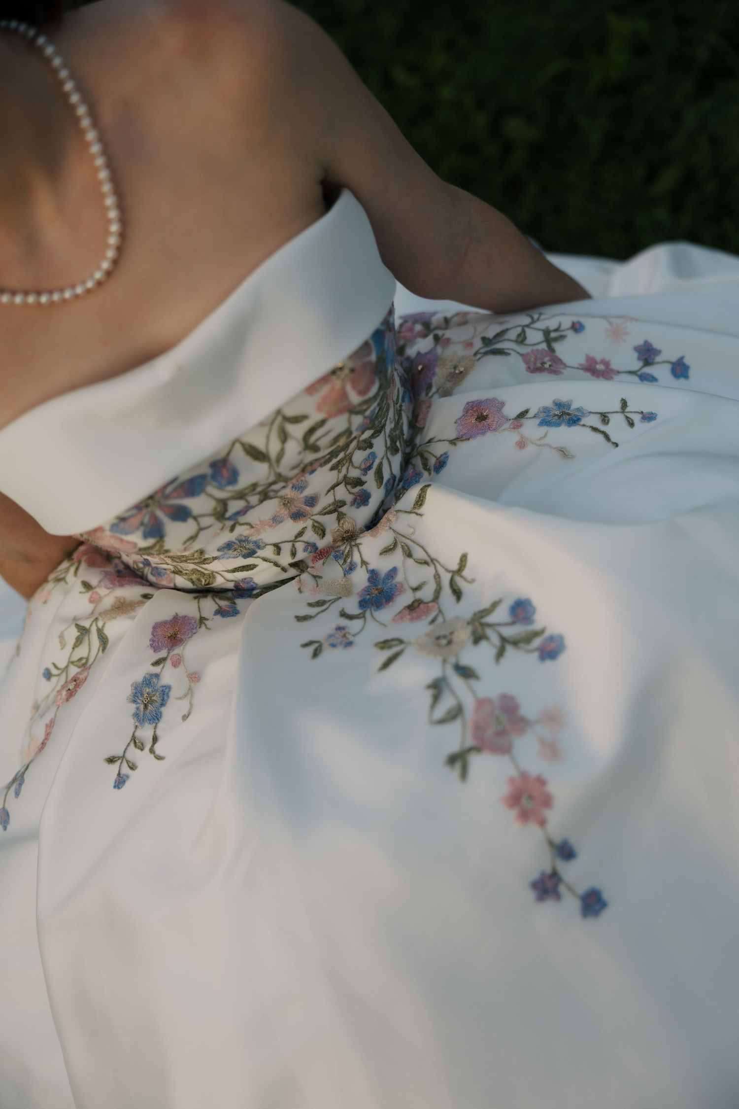 Close-up of a white wedding gown with delicate floral embroidery and a pearl necklace accessory.