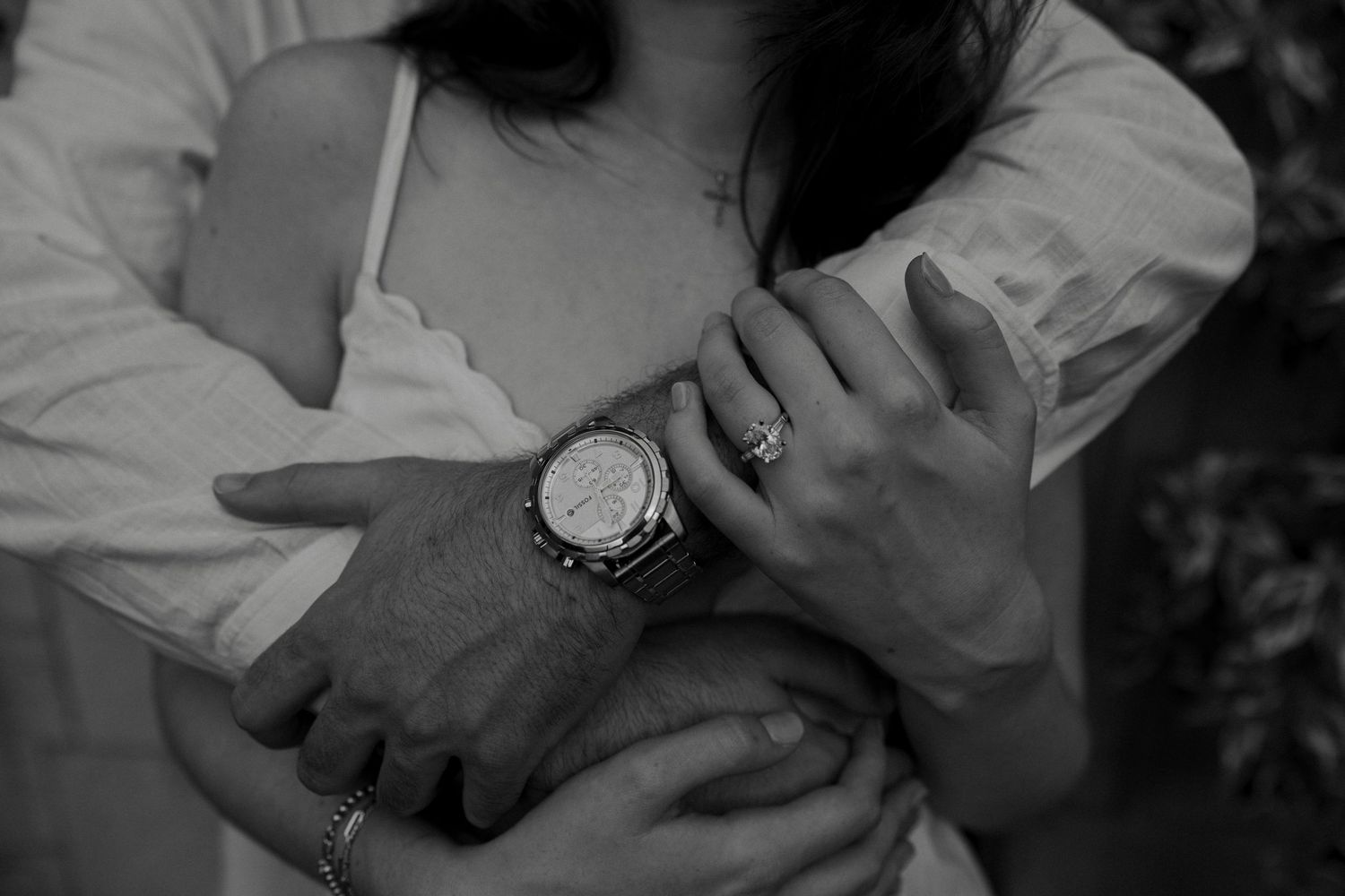 Close-up black and white photo of couple embracing showing engagement ring and watch.