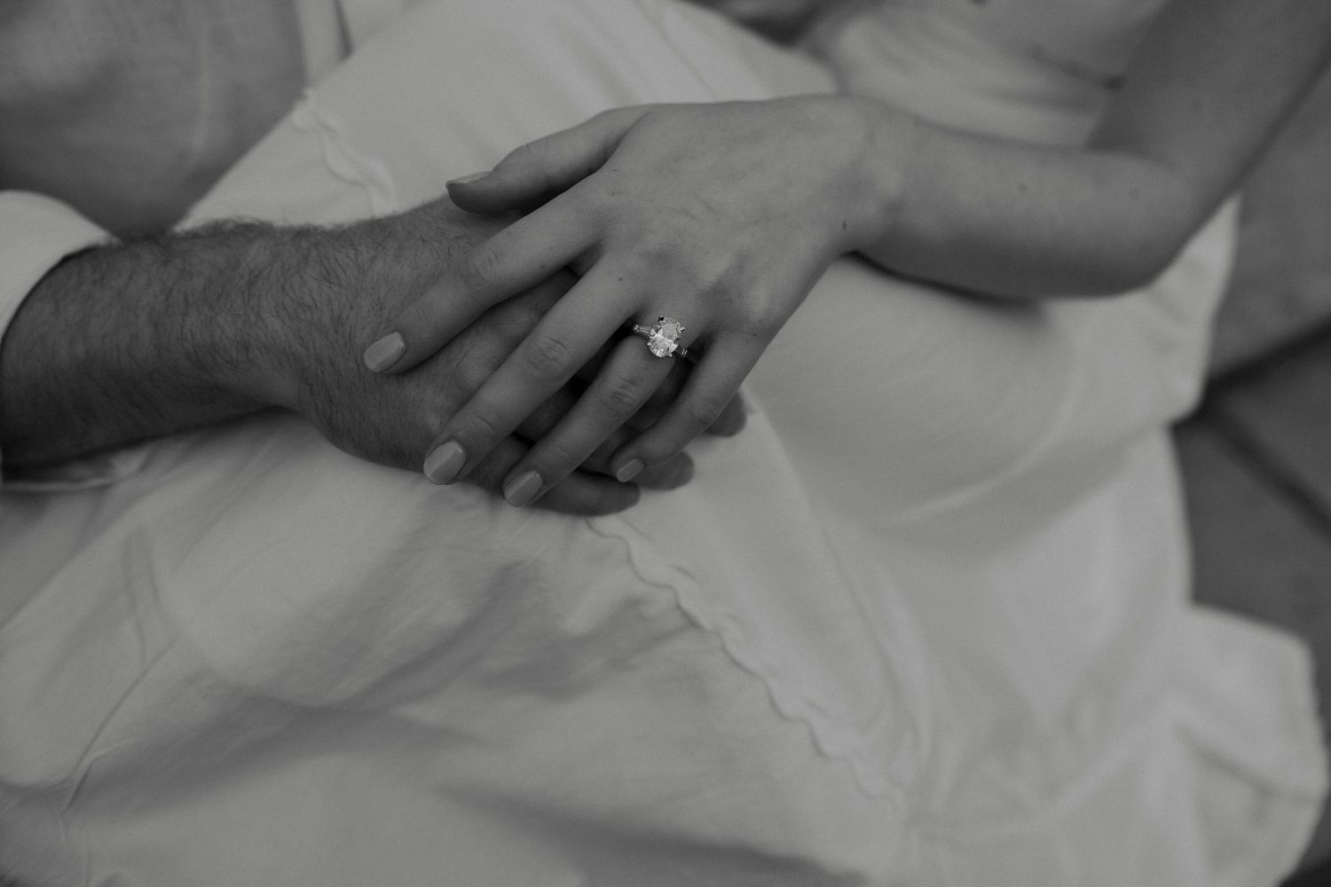 Black and white photo of couple holding hands showing engagement ring on wedding day.