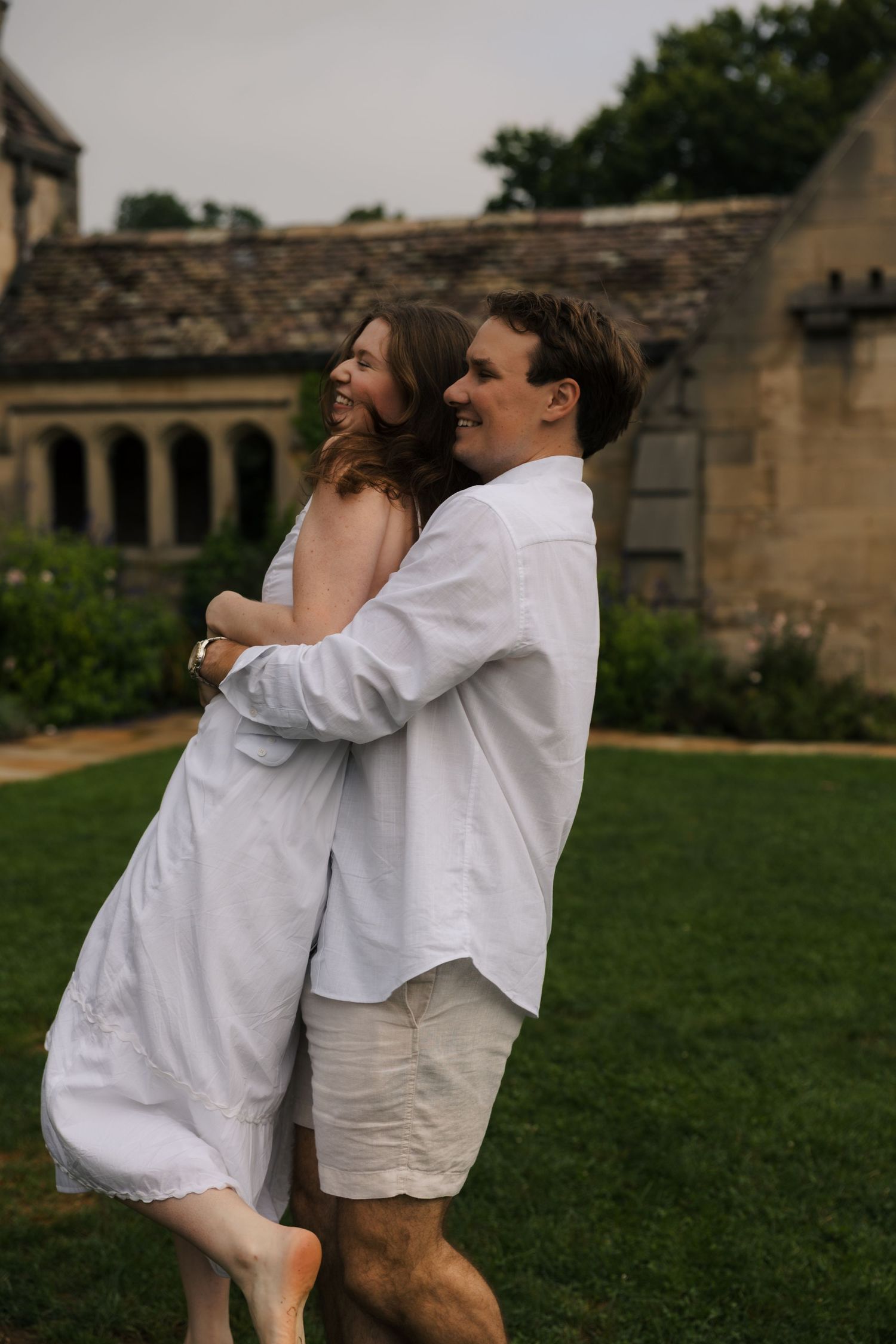 Happy couple embracing and spinning on green lawn in front of a beautiful historic stone estate.