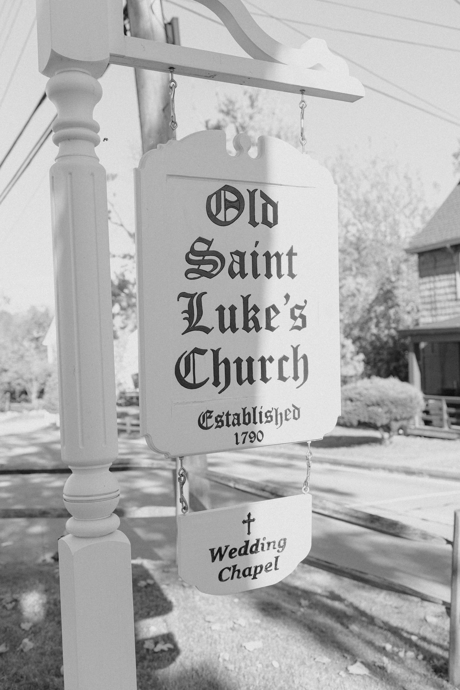 Black and white sign for Old Saint Luke's Church, established 1790, with a Wedding Chapel placard hanging below.