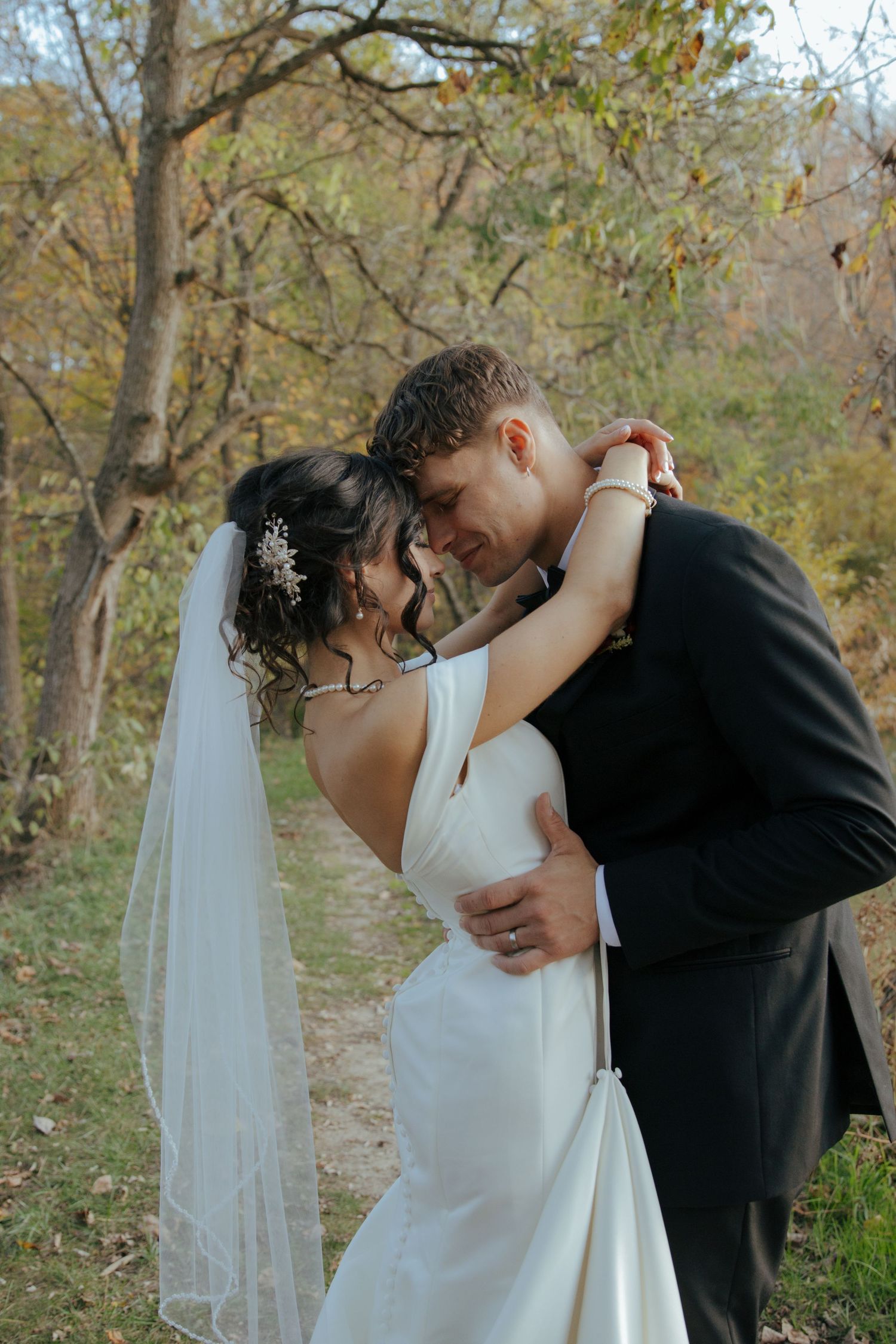 Bride and groom touch foreheads tenderly in a romantic outdoor portrait surrounded by fall foliage.