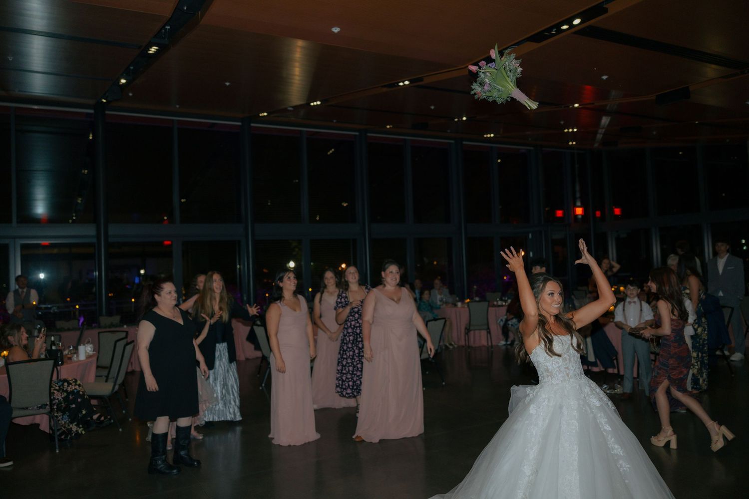 Bride tossing bouquet to bridesmaids in pink dresses at elegant wedding reception venue.