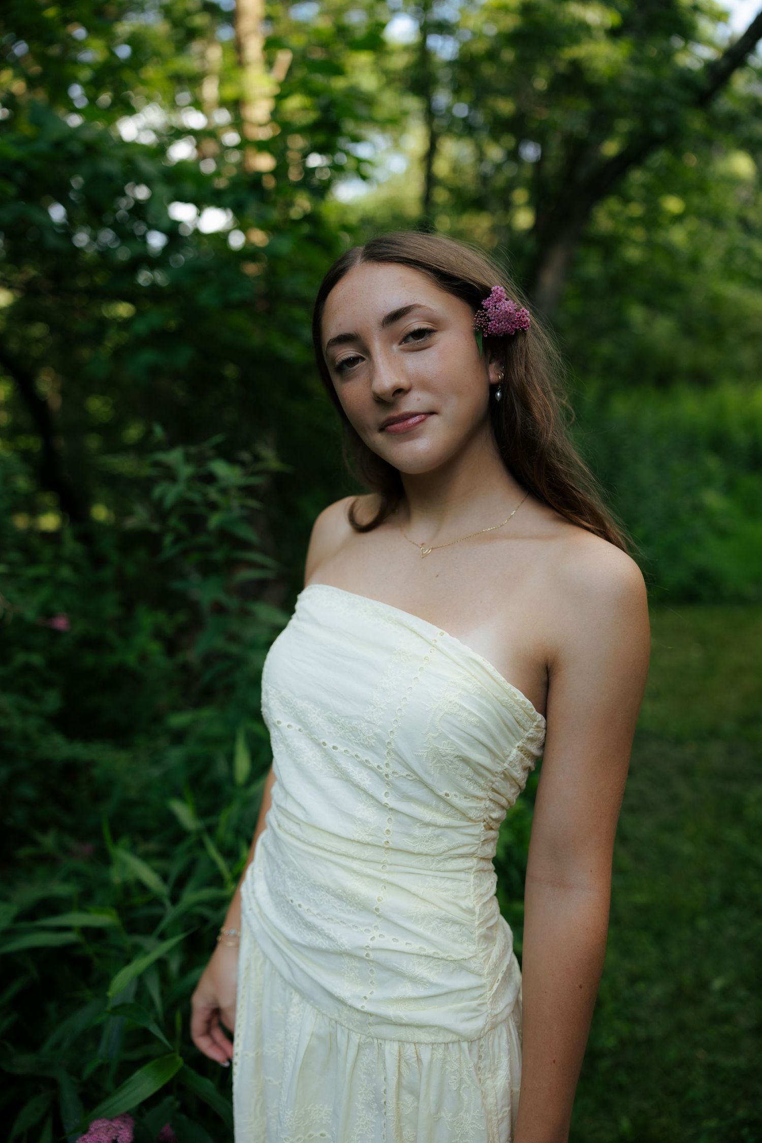 Young woman in white strapless dress with pink flower in hair outdoors.
