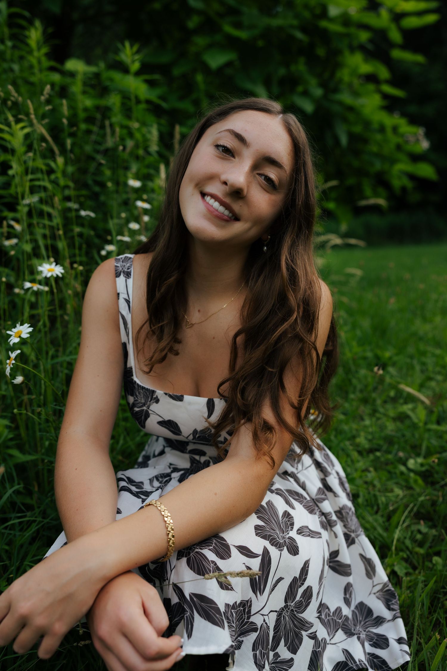 Young woman in floral dress sitting in green grass smiling.