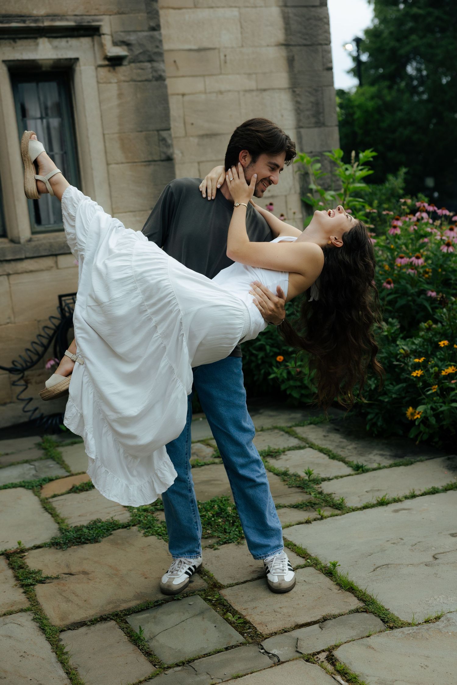 A man in jeans dips a woman in a white dress during a romantic outdoor photo session.