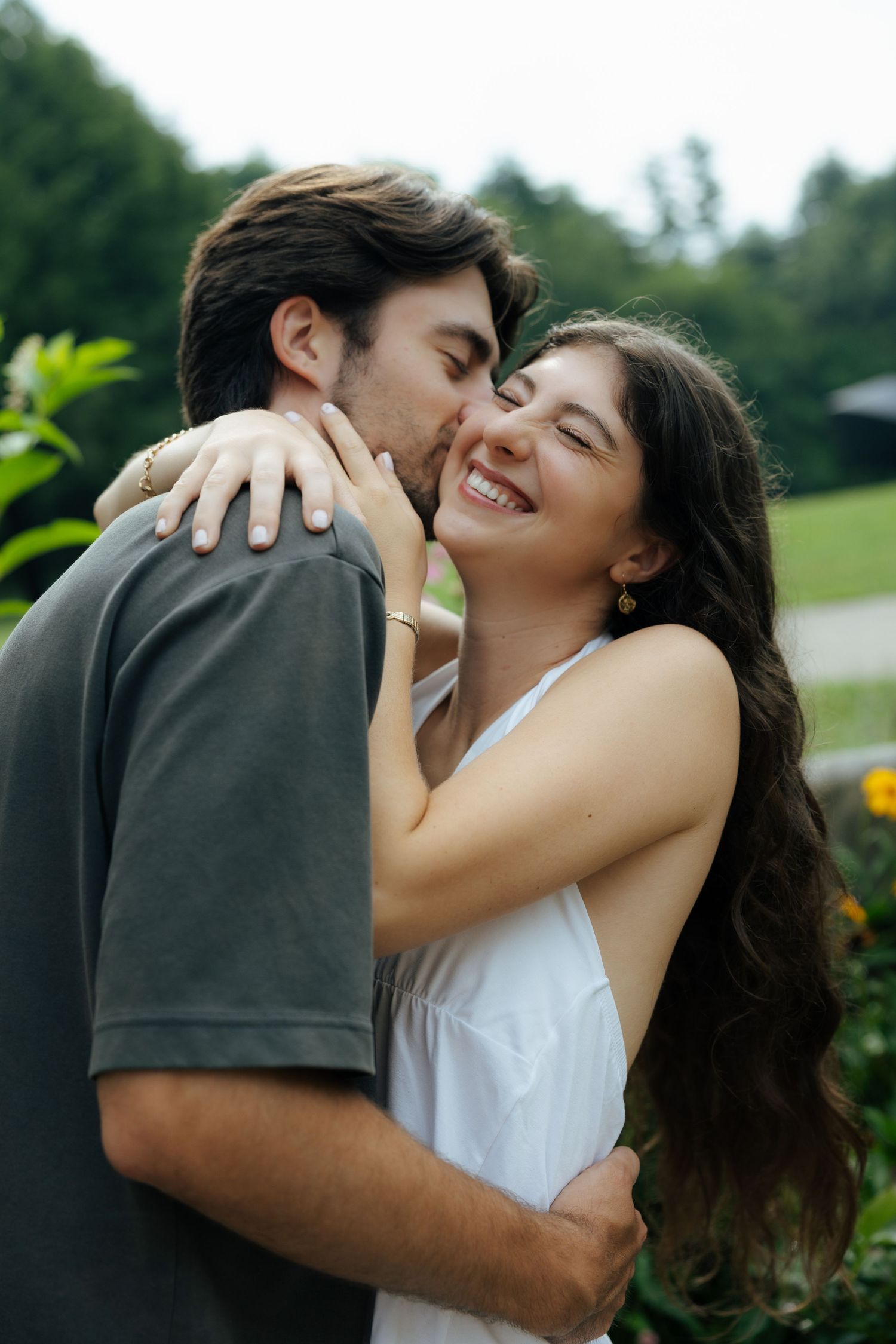 Couple sharing a romantic moment as man kisses womans cheek while she smiles in a garden setting.
