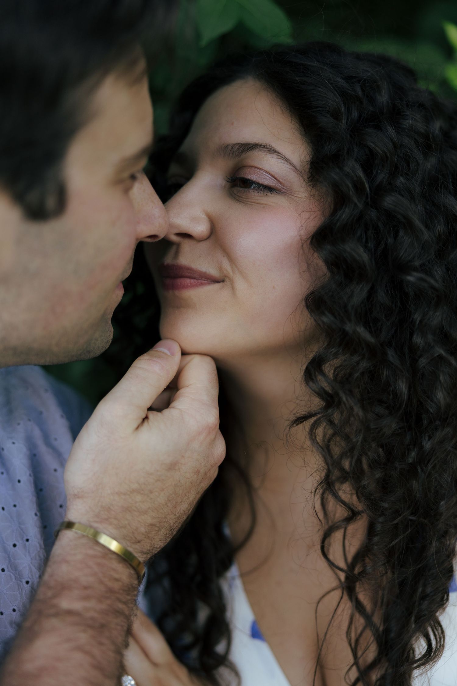 Man gently kissing womans cheek while holding her chin in romantic outdoor portrait.