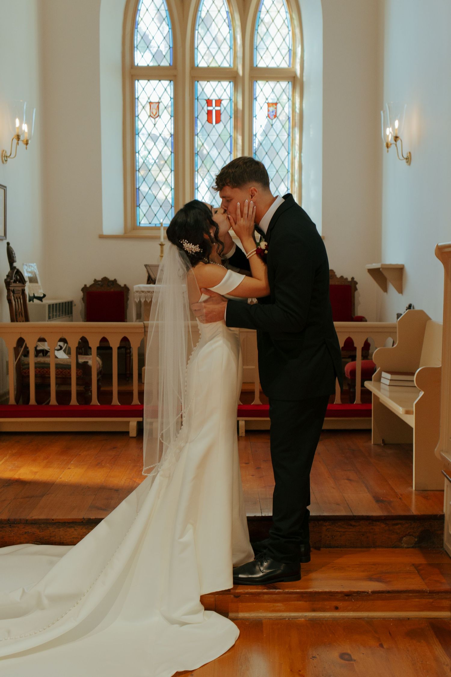 Bride and groom share their first kiss at the altar of a charming church with stained glass windows.