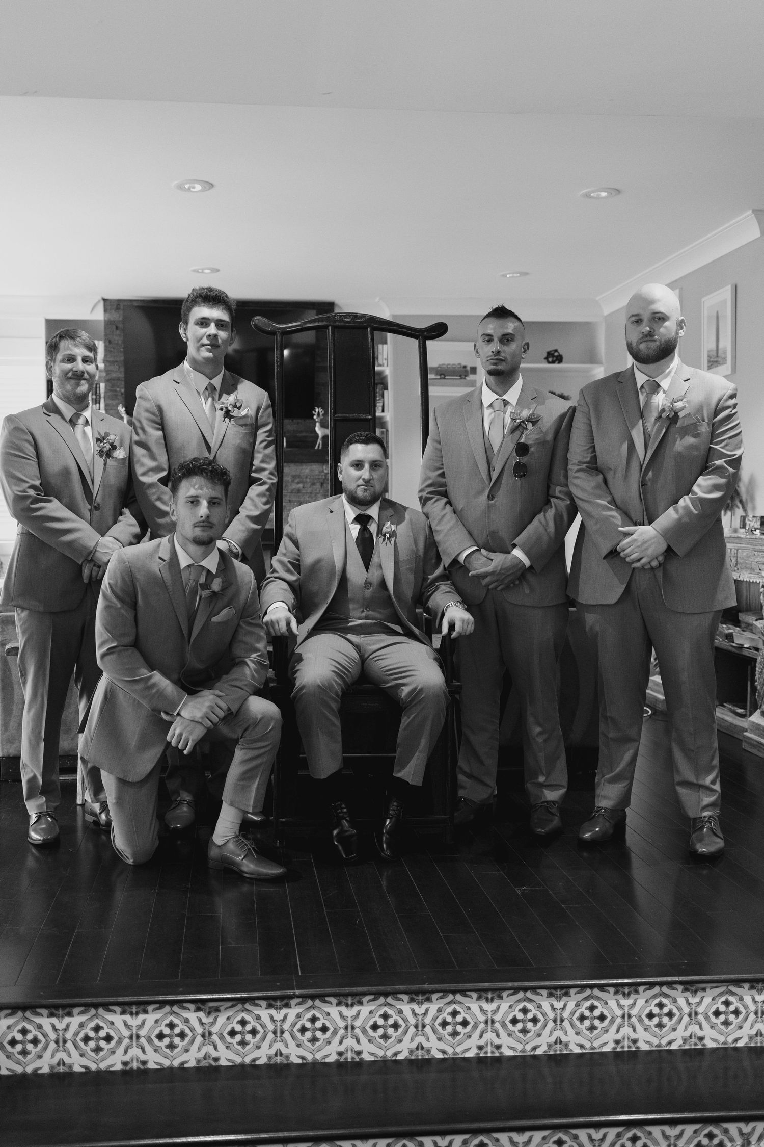Black and white photo of groom and groomsmen in suits posing together indoors before a wedding ceremony.