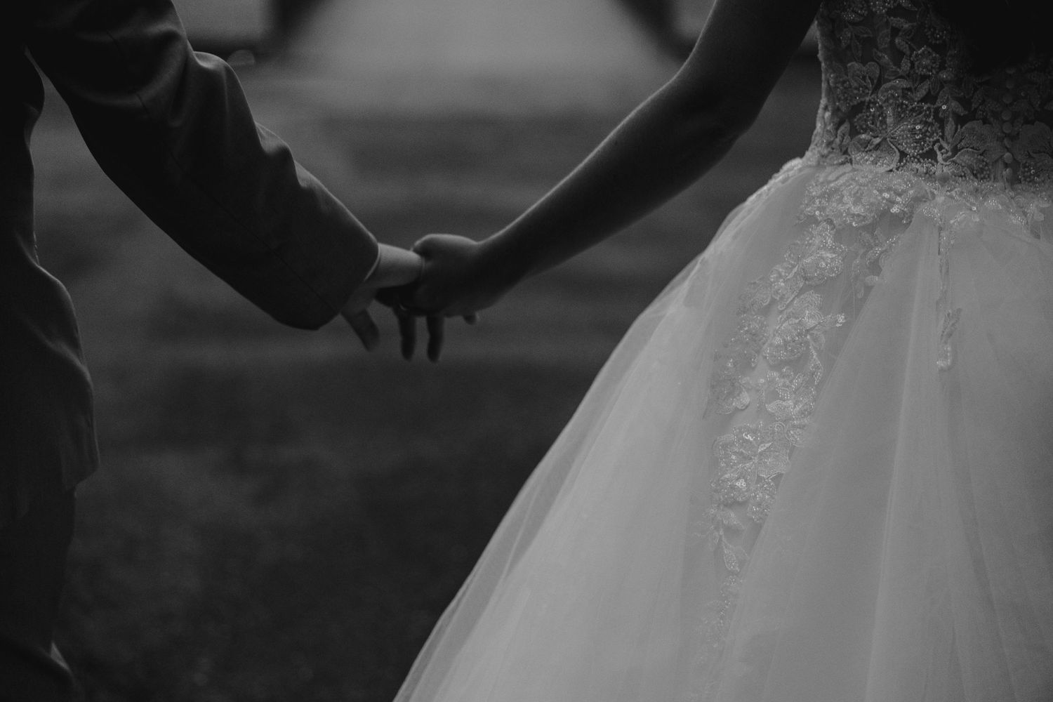 Black and white wedding photo of bride and groom holding hands, showcasing lace bridal gown detail.