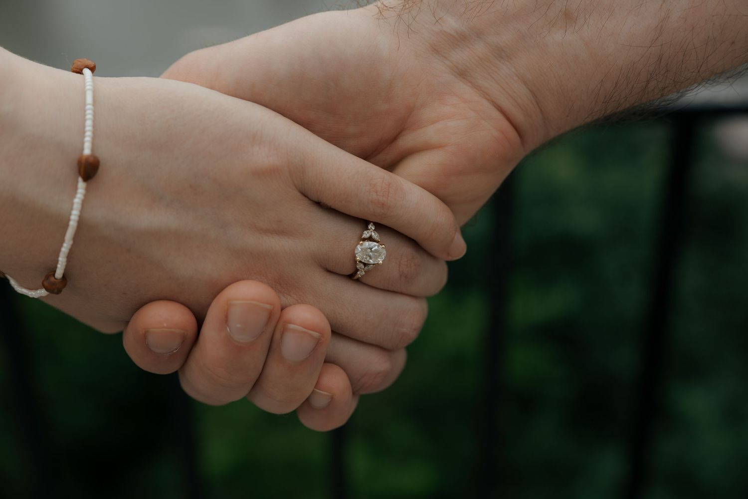 Two hands holding, one wearing a diamond engagement ring and a delicate bracelet, symbolizing love and commitment.