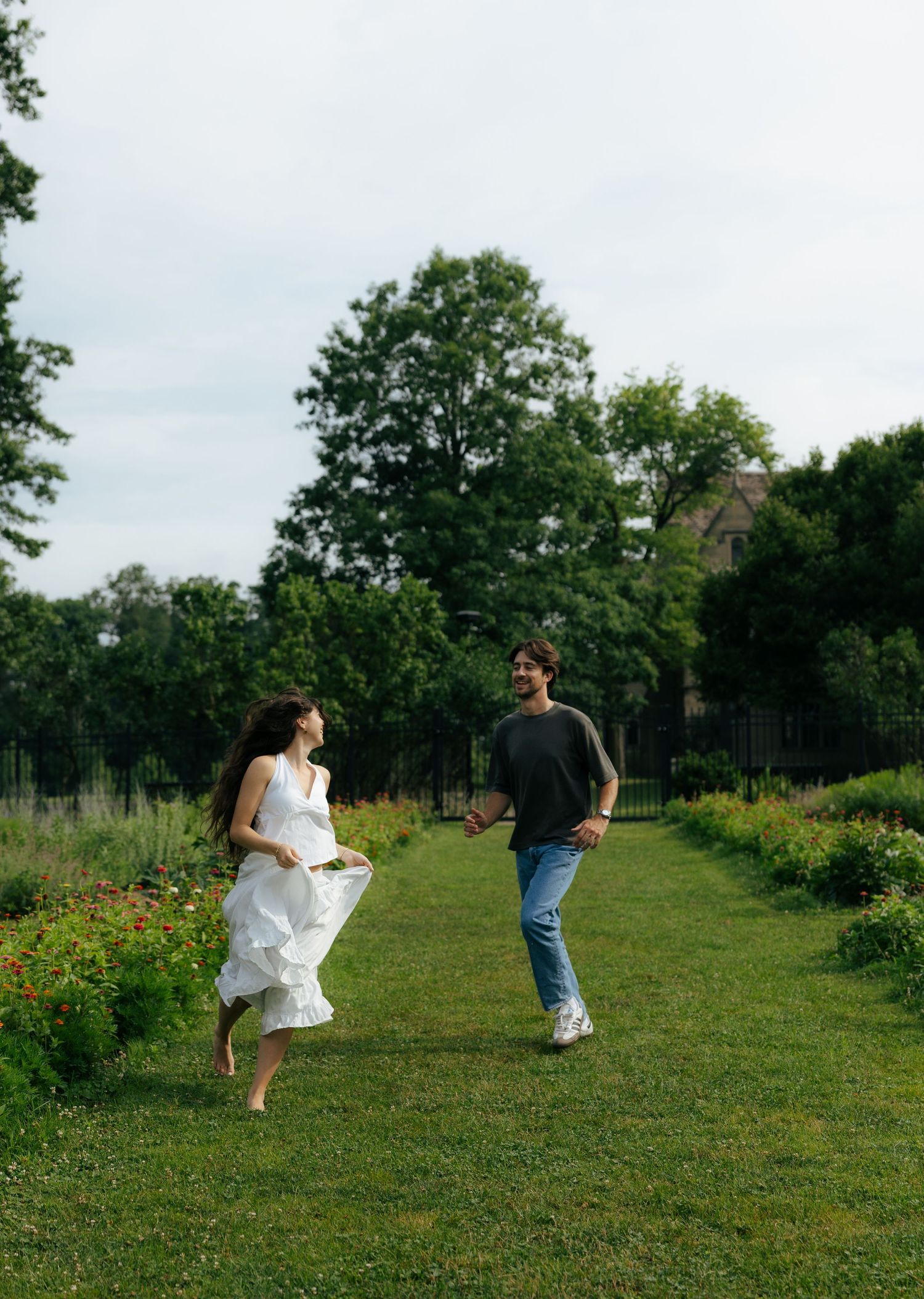 Joyful couple running toward each other on a green garden path, woman in white dress, man in jeans and gray shirt.
