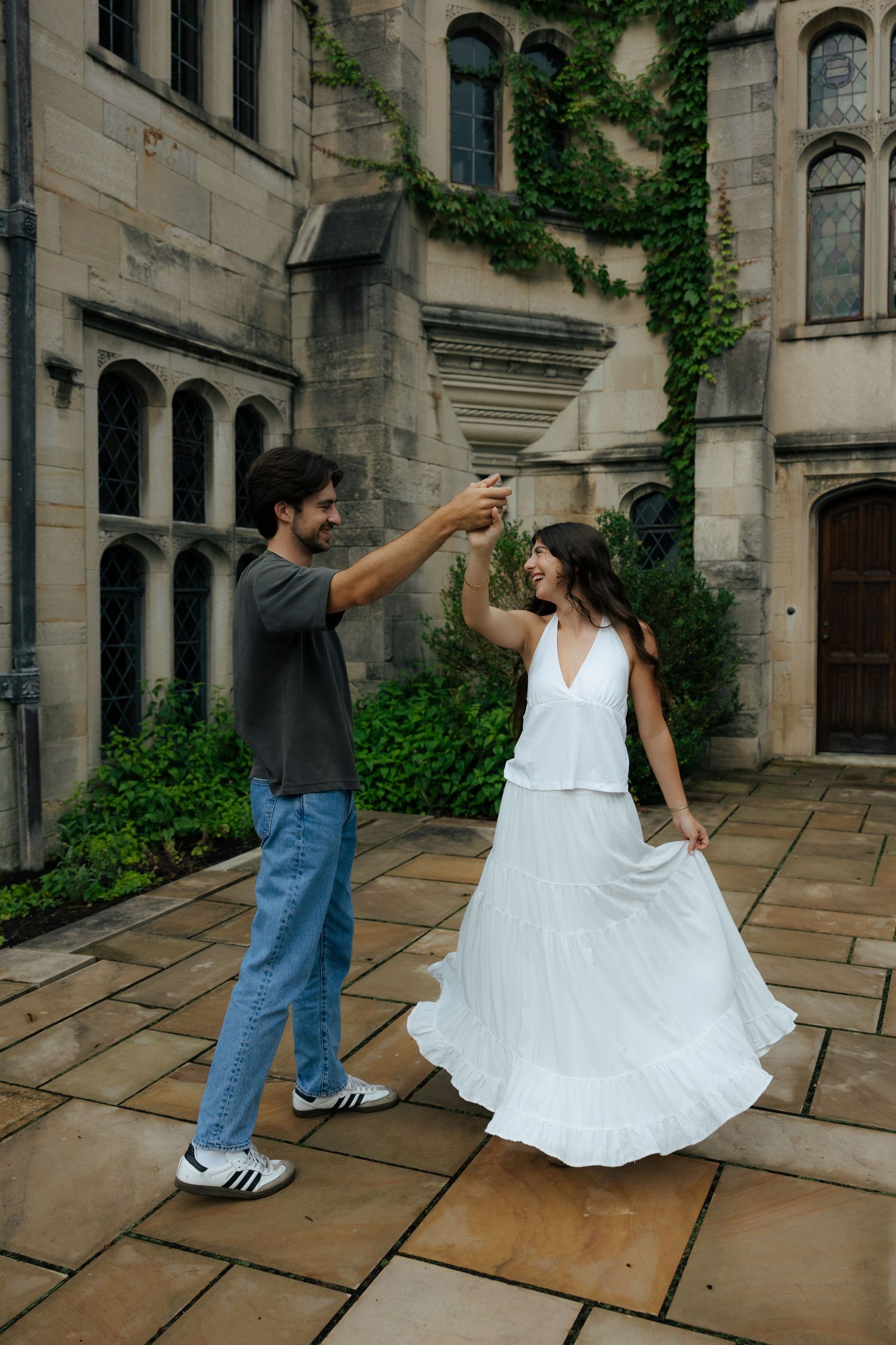 A joyful couple dances in a courtyard of an ivy-covered stone building, the woman wearing a white dress.