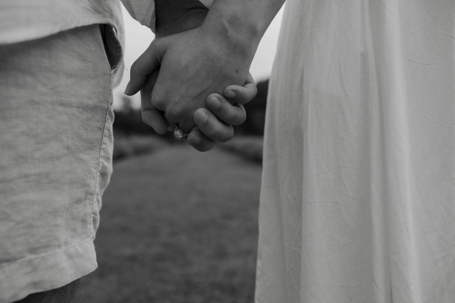 Black and white close-up of a couple holding hands, one in a white dress, symbolizing love and togetherness.