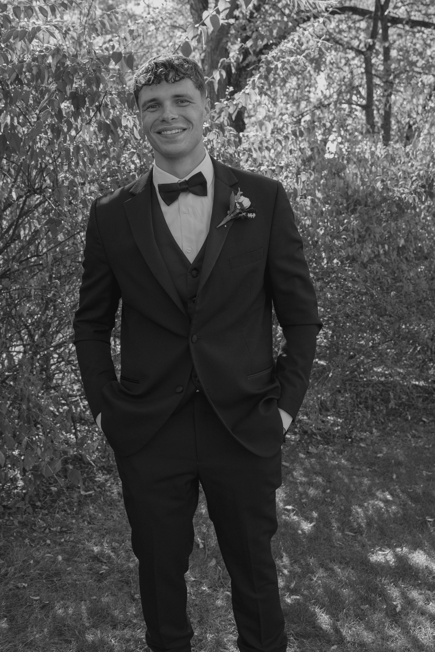 Black and white photo of smiling young man in black tuxedo with boutonniere.