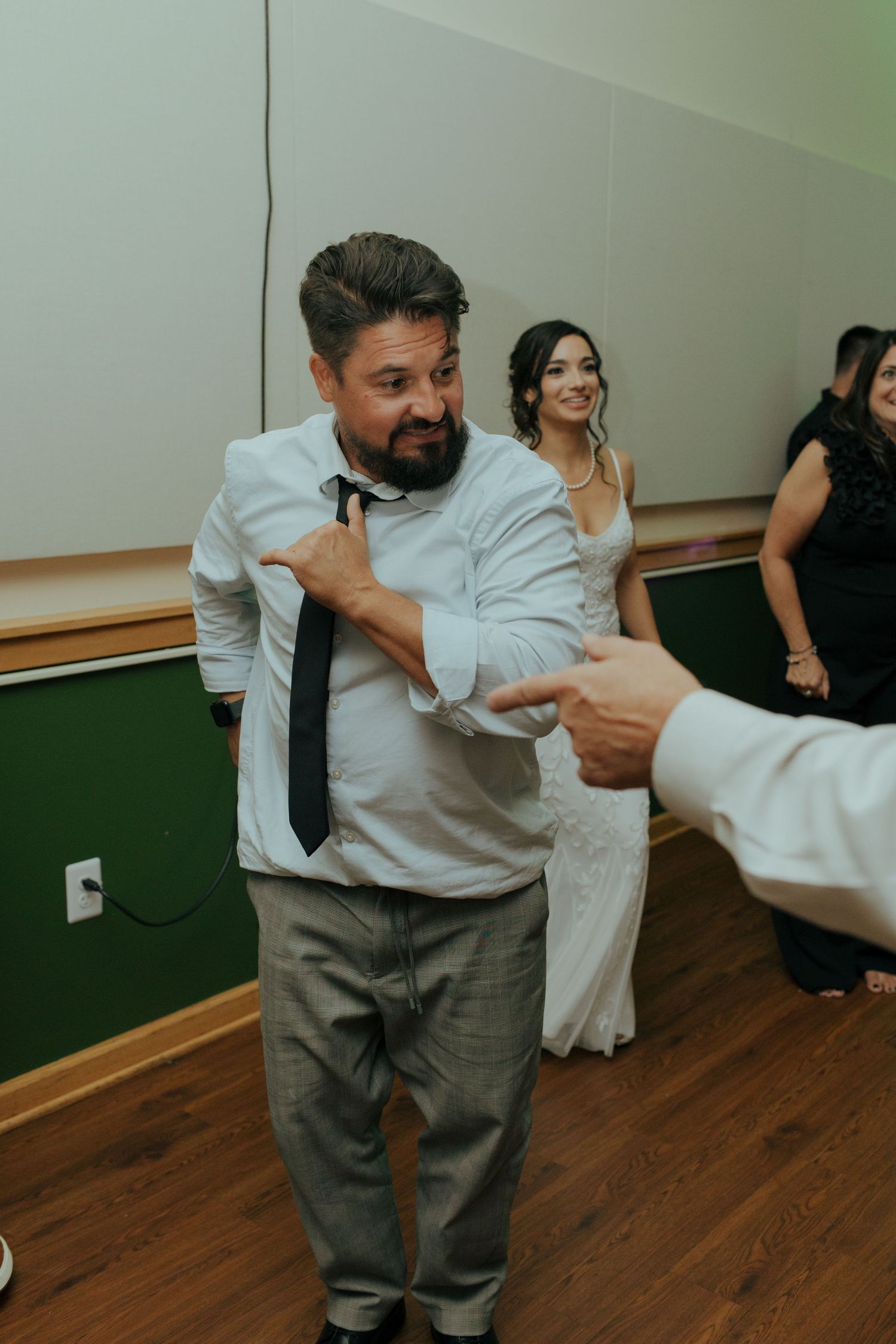 Male wedding guest dancing energetically on reception dance floor with bride in background.
