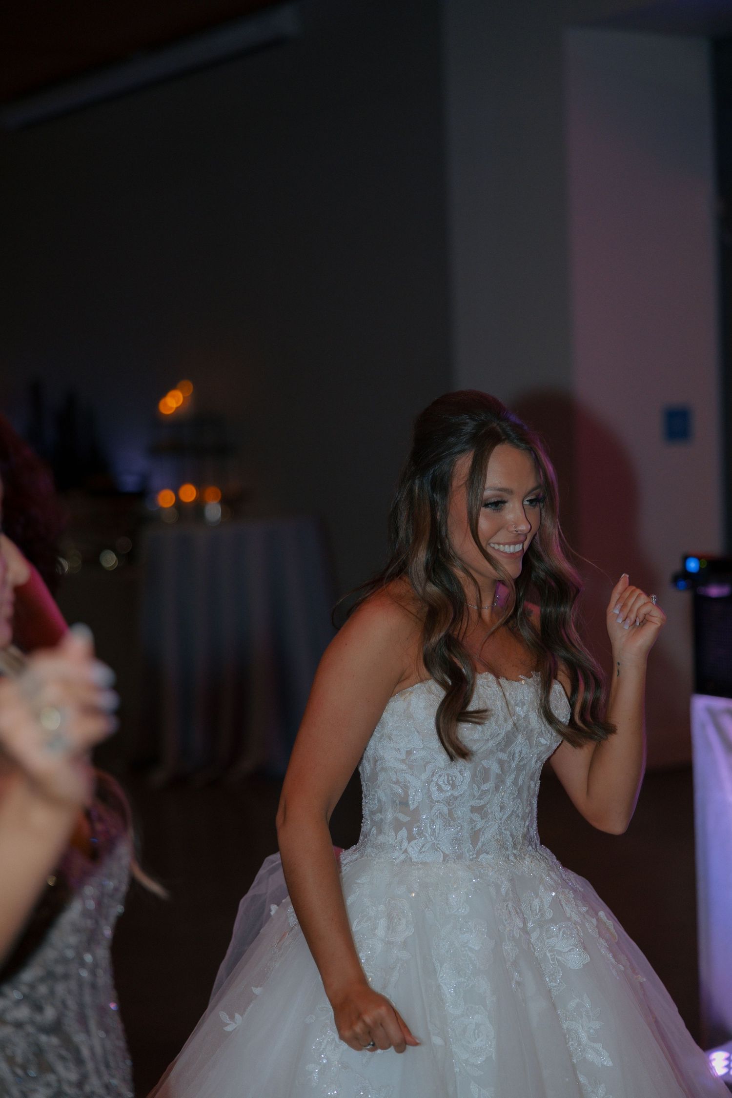 Bride in a strapless lace ballgown laughing and dancing joyfully at her wedding reception.
