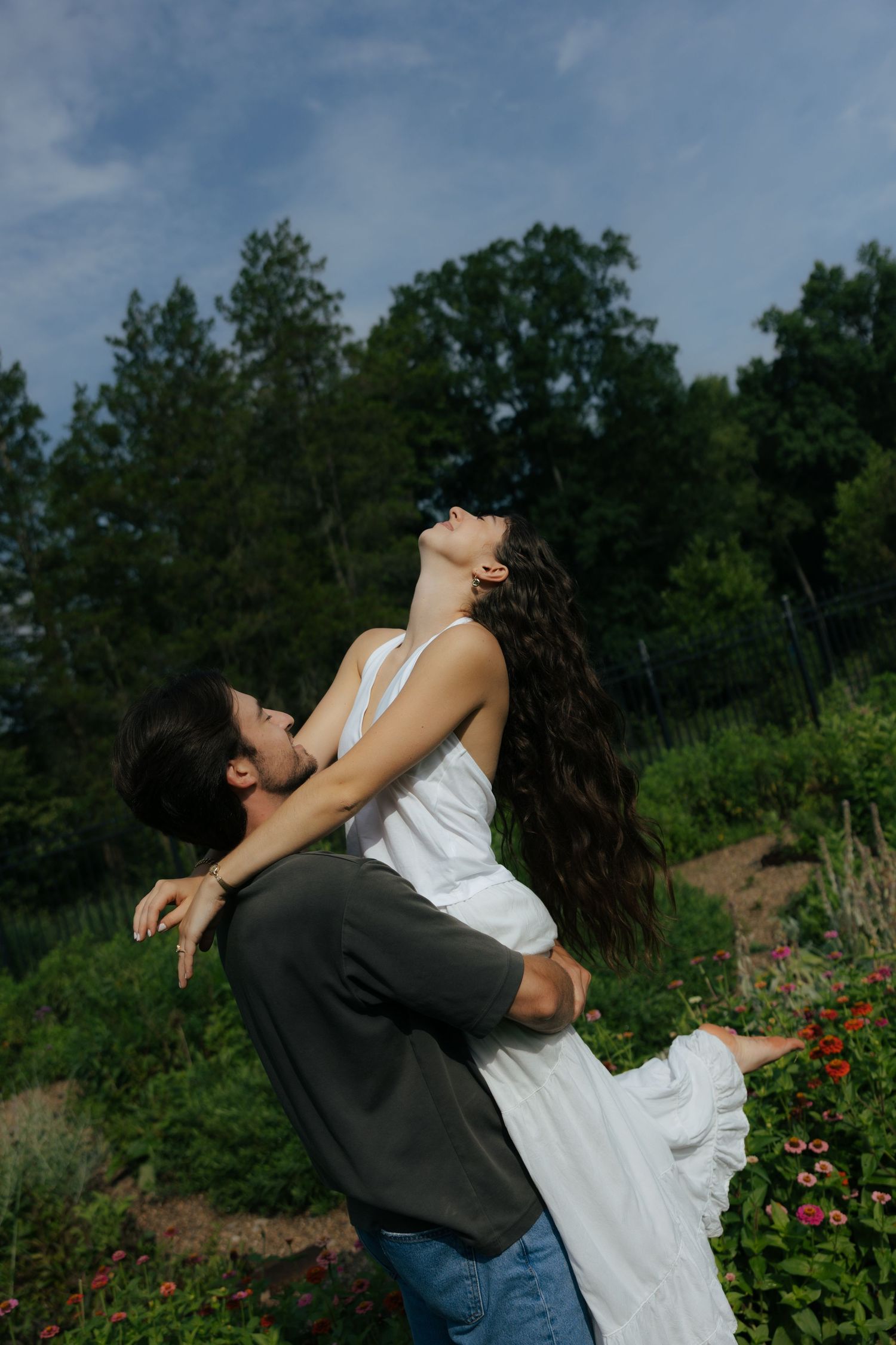 A romantic couple shares an intimate moment outdoors, the man lifting the woman in a white dress as she tilts her head back.