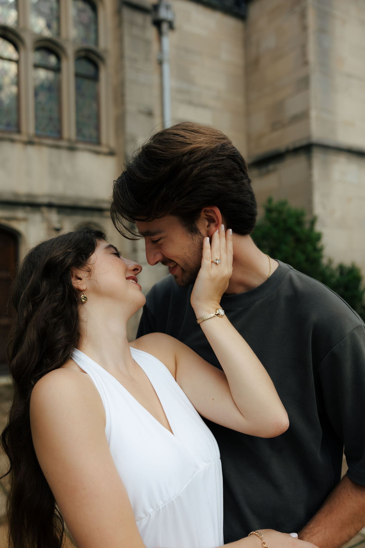 A couple shares a romantic moment, the woman in a white dress touching the man's face as they lean in close.