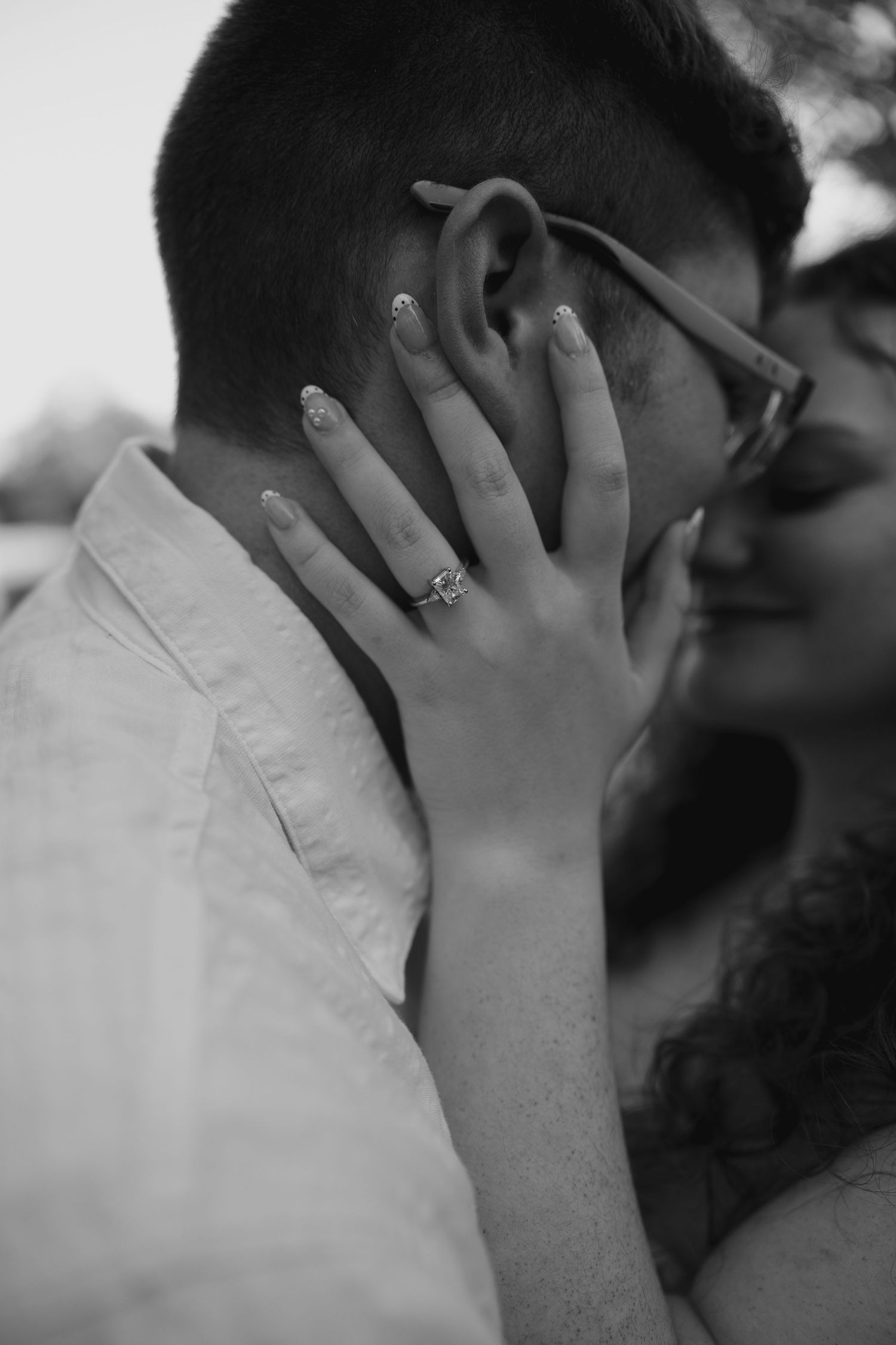 Close-up black and white photo of an engagement ring on a woman's hand touching her partner's face.