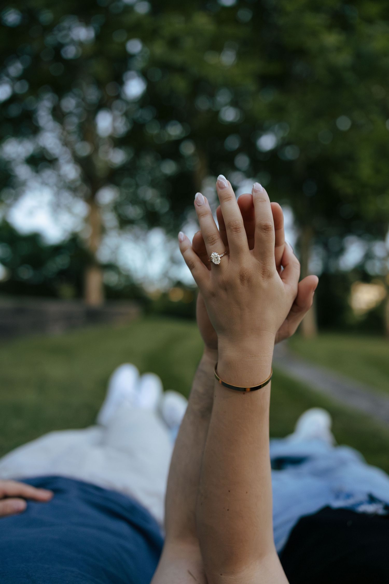 Close-up of a woman's hand displaying an engagement ring while holding hands with her partner in a park.