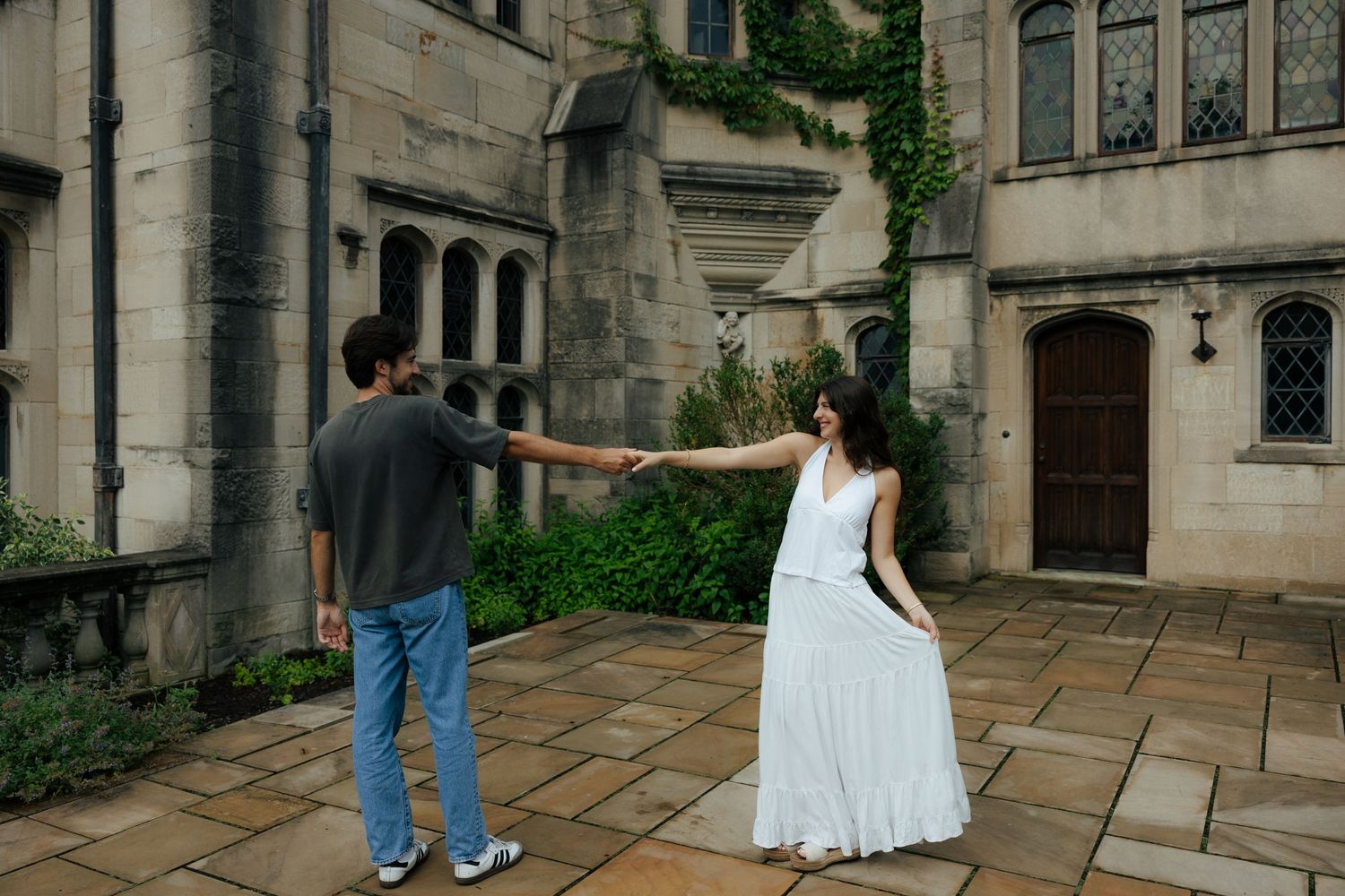 A couple dances together on a stone patio outside a historic ivy-covered building.