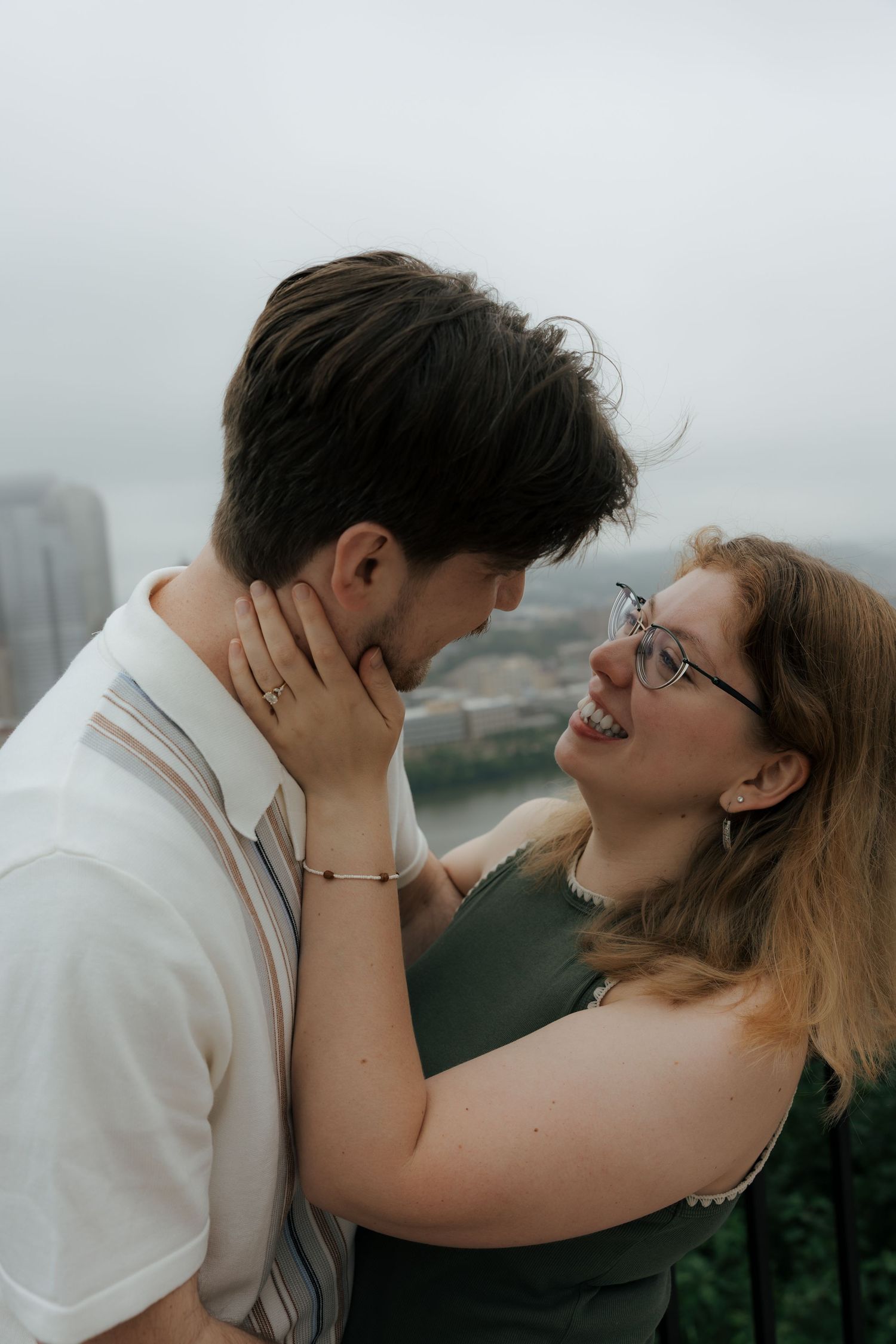 Young couple sharing a romantic moment on a rooftop balcony, woman smiling warmly while cradling mans face.
