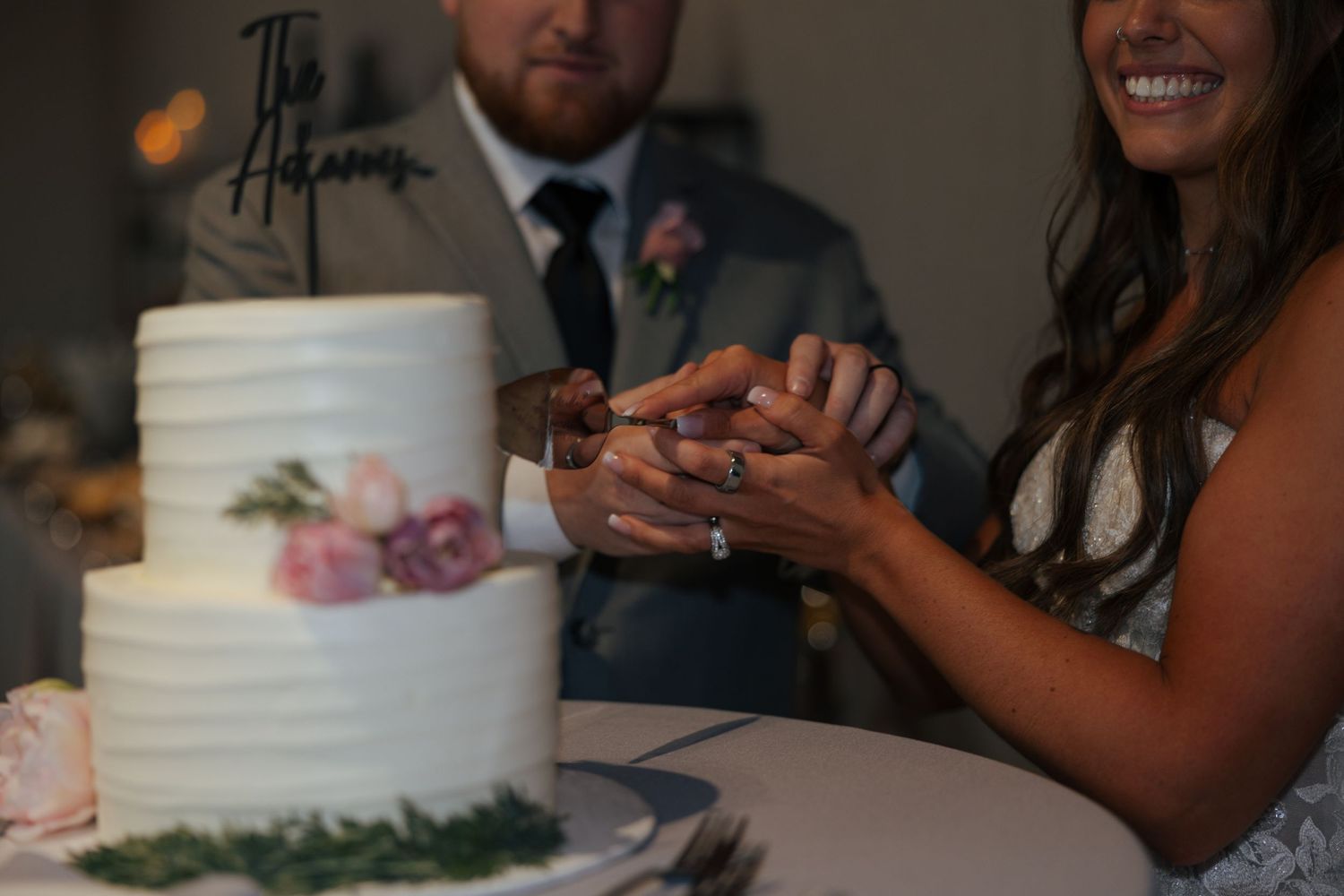 Bride and groom cutting a two-tier white wedding cake with floral decor and personalized topper at their reception.
